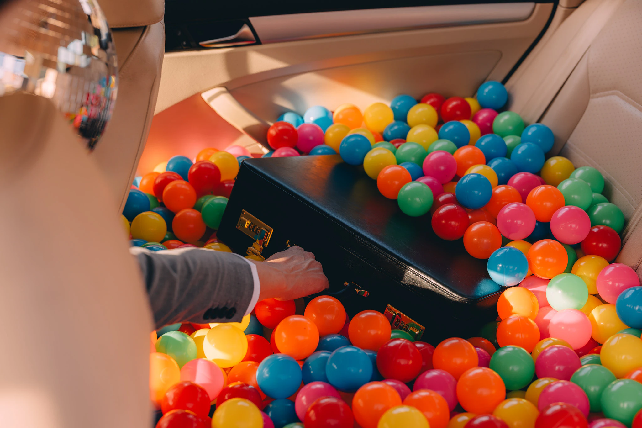 Person in a suit and disco ball for a head reaching into a ball pit in the back seat for a briefcase. For Internal Use Only from Jonathan Grado's Happy Hour series.