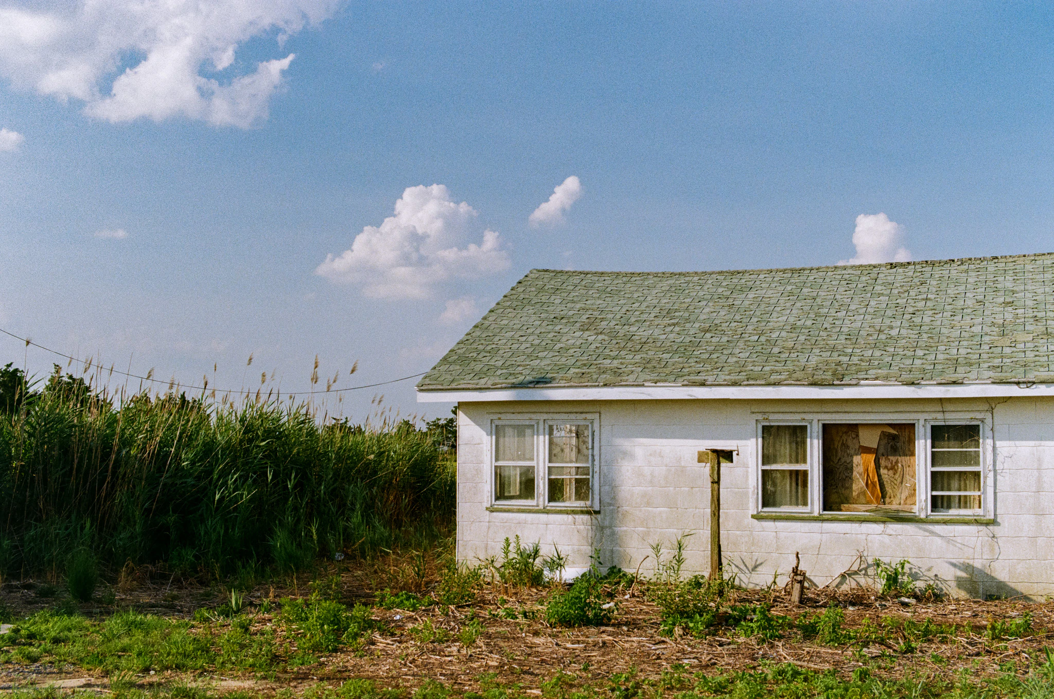 Abandoned house in a field under puffy clouds on gold 200 film