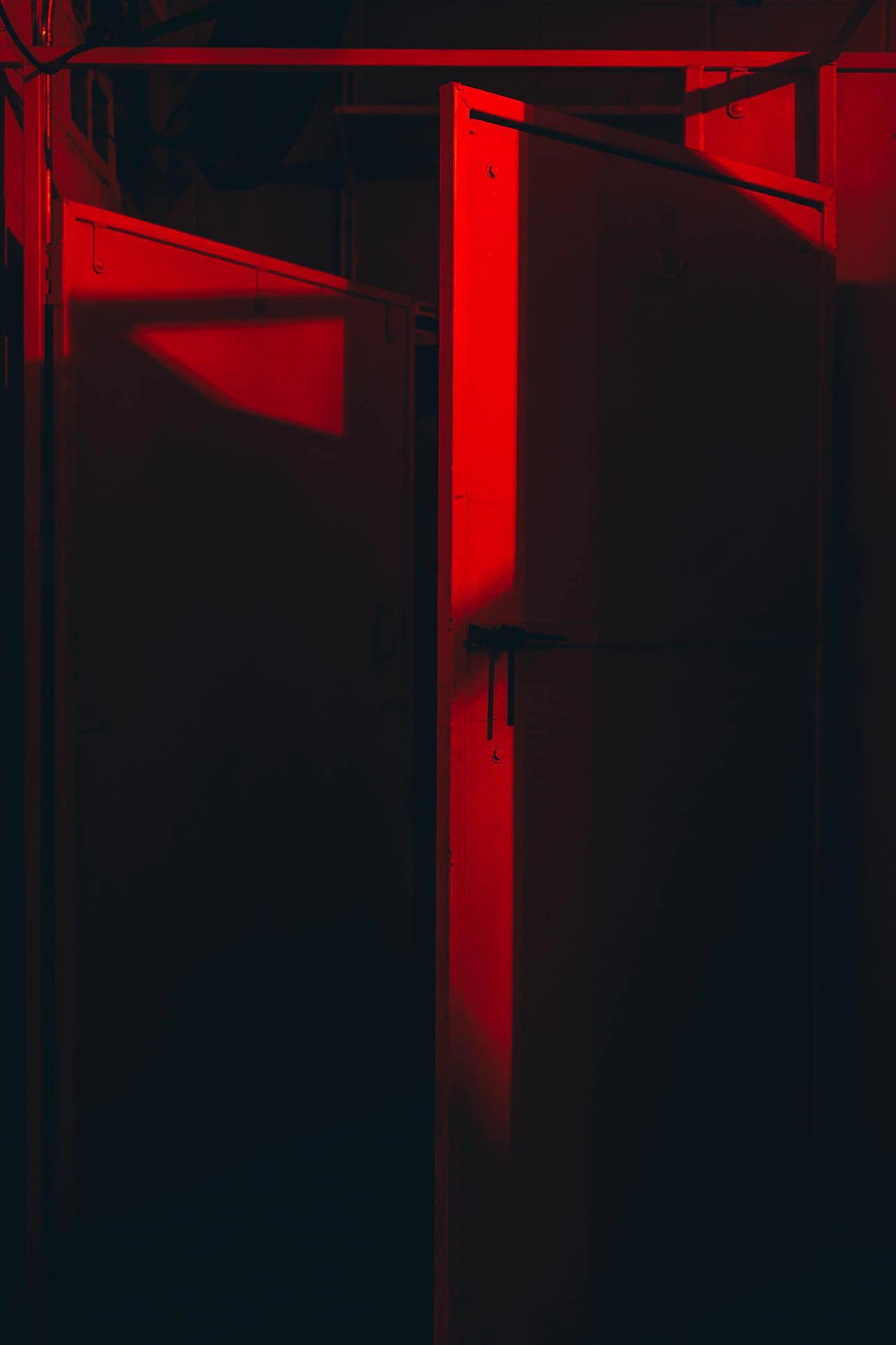 A slightly open bathroom stall in a red lit bathroom at night. Red Bathroom #01 from Jonathan Grado's Hold Down to Flush.