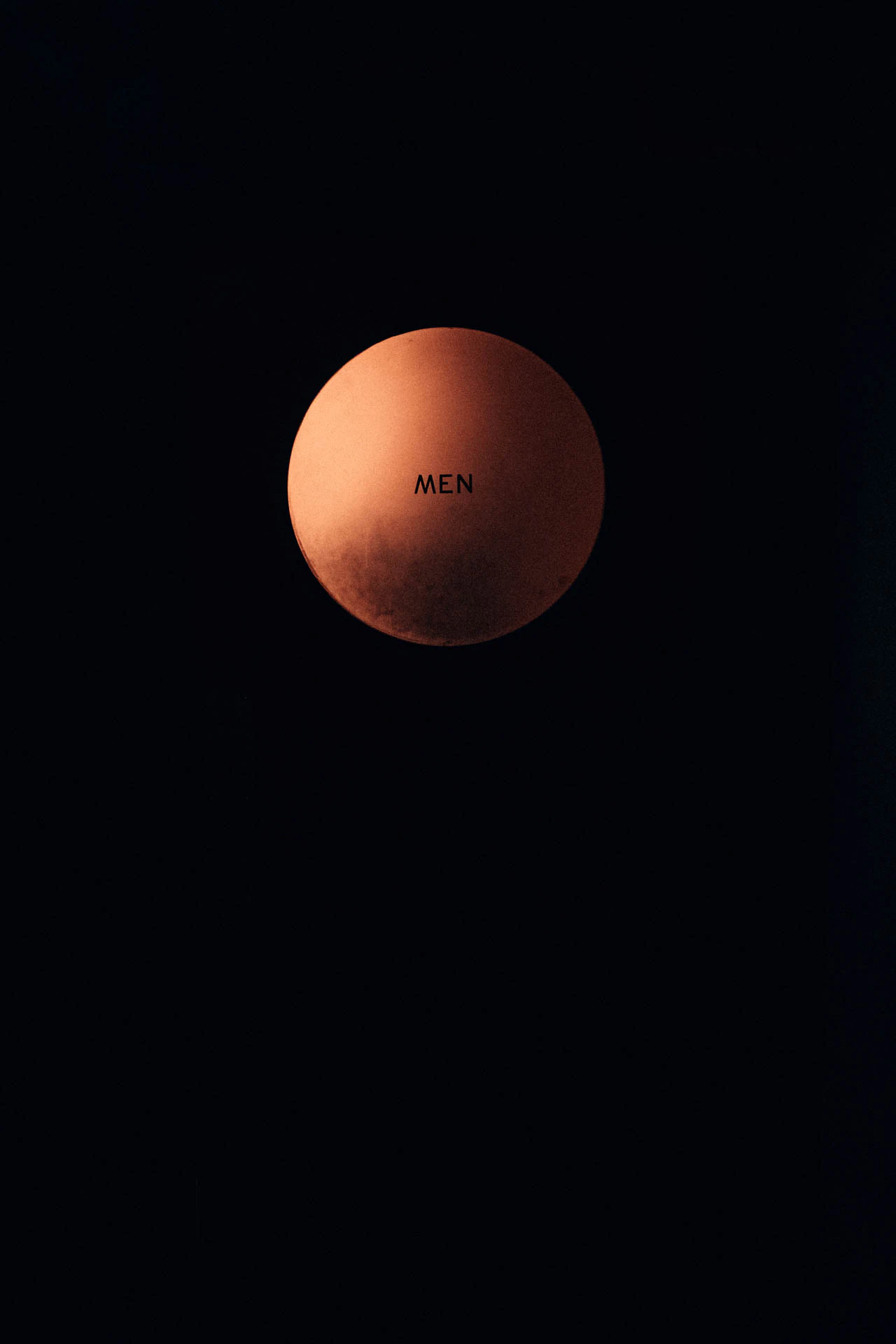 The word MEN on a moon-like glass circle on a bathroom door. MEN from Jonathan Grado's Hold Down to Flush.