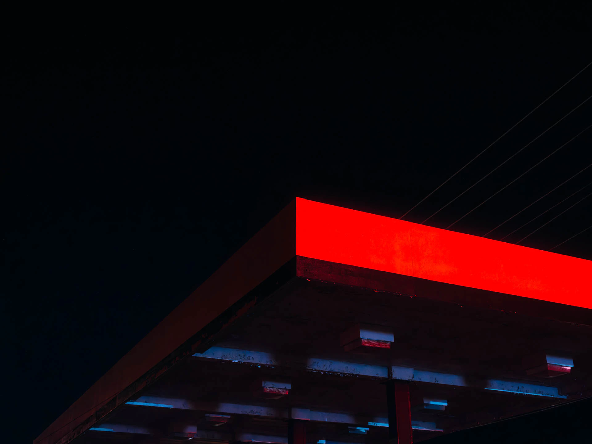 The roof of a gas station lit by a red neon sign at night