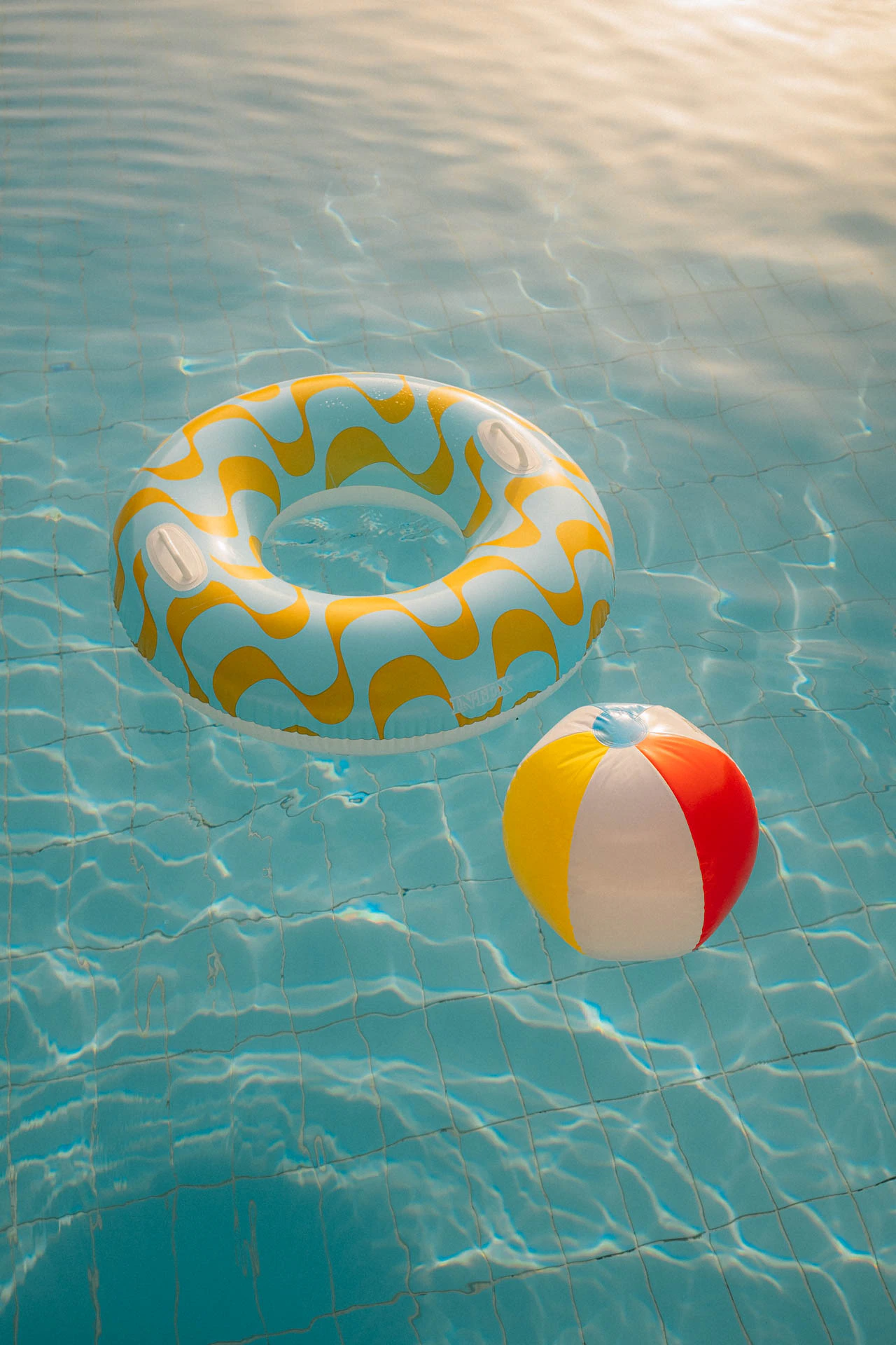 Beach ball and donut floating in a pool at sunset