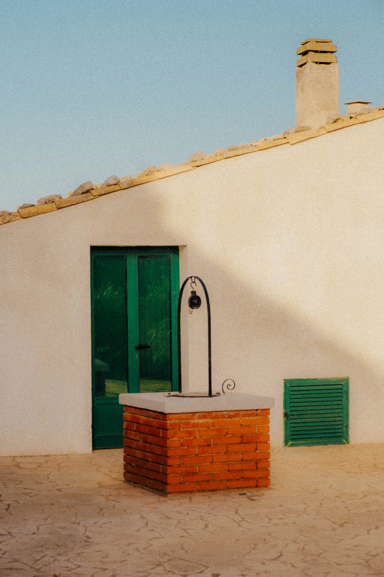 A house in Sicily with green doors and a red brick well