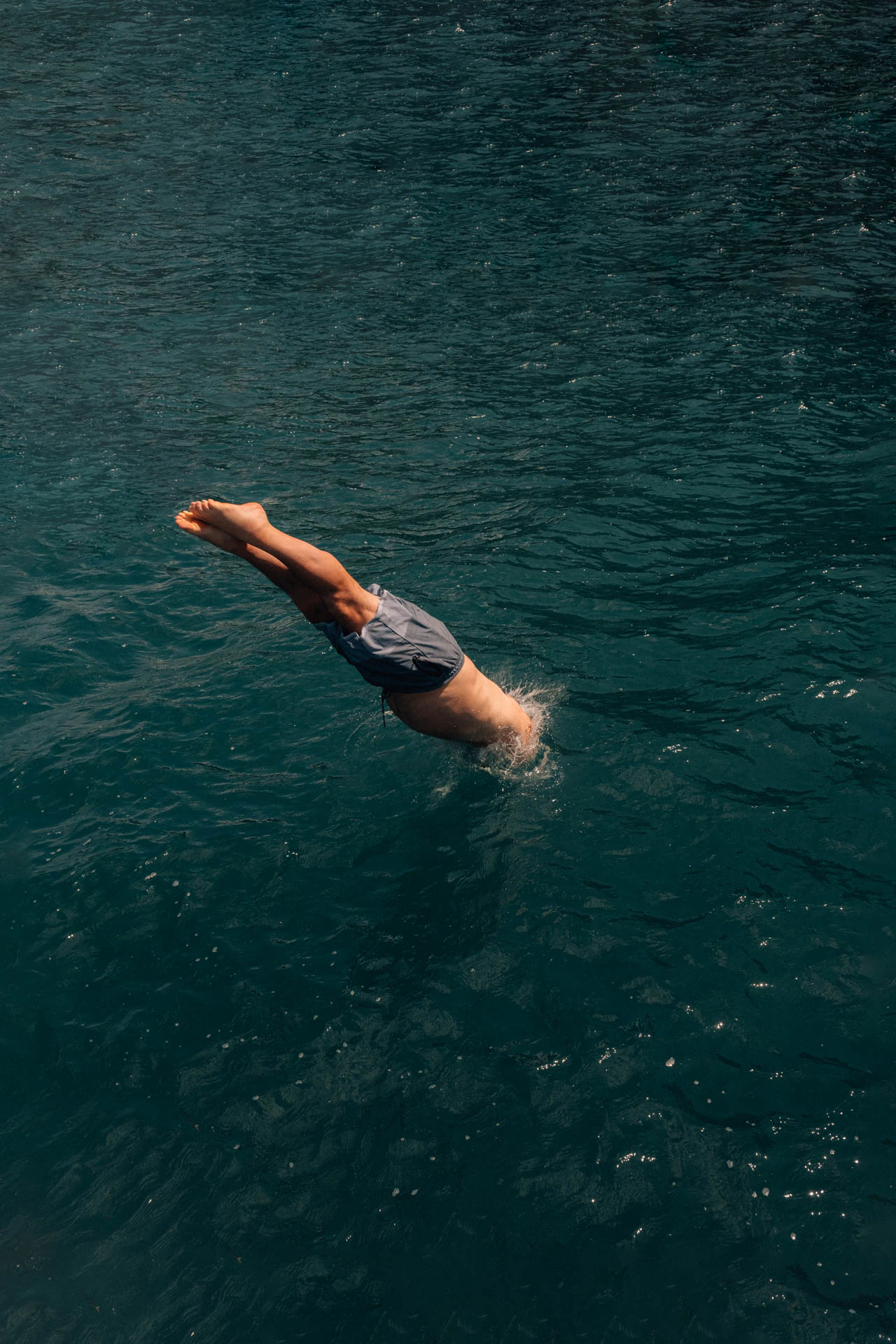 A man diving into the ocean head first from a boat. Only his body and legs are visible