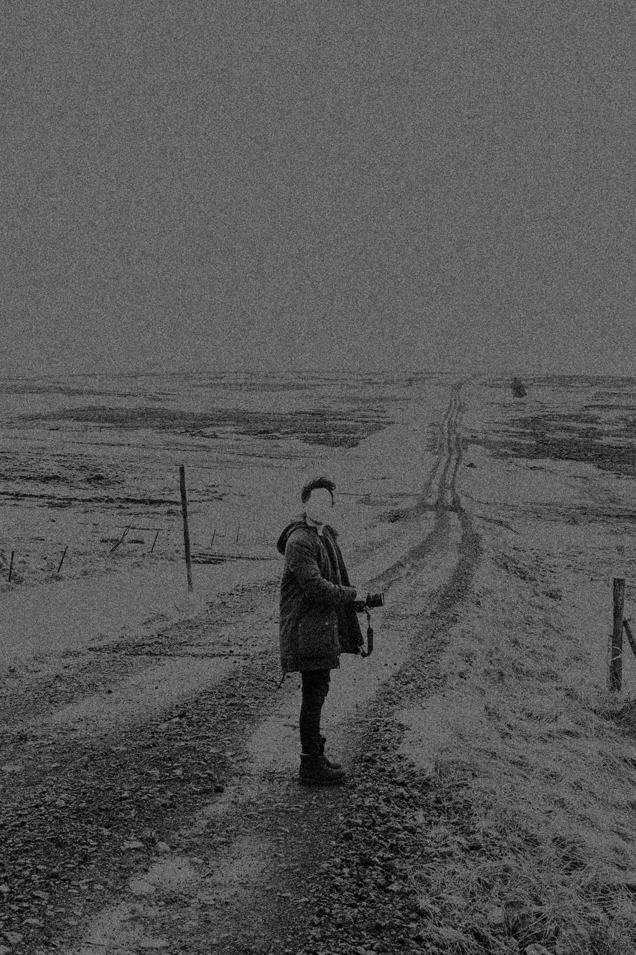 Faceless man standing on a long stretch of road in Iceland. Looking Back from Jonathan Grado's Dirty Static.