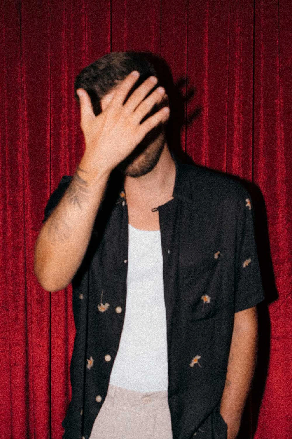 Jonathan Grado with his hand in front of his face on red velvet and high flash