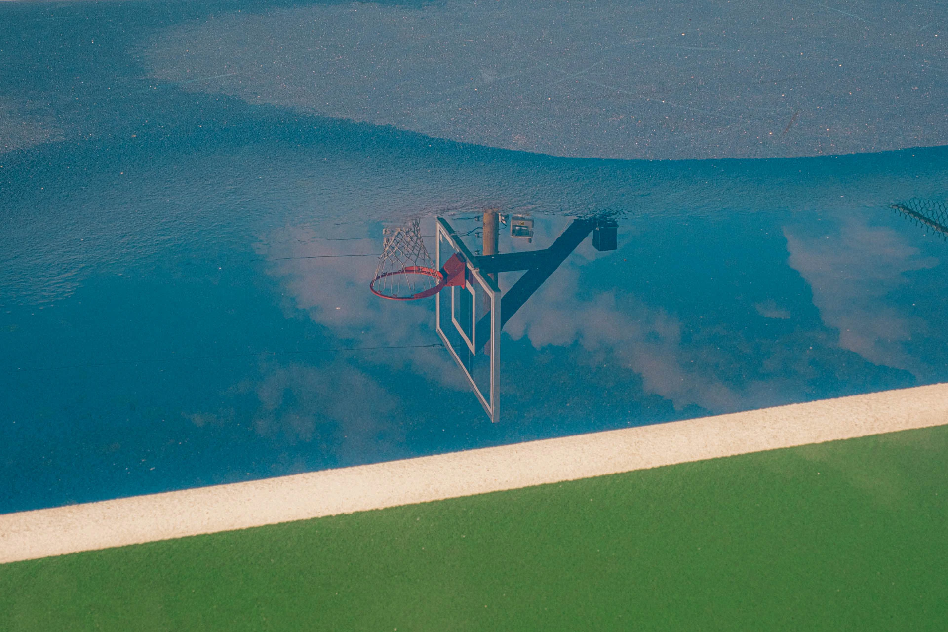 basketball hoop in the reflection of a rainy blue and green court