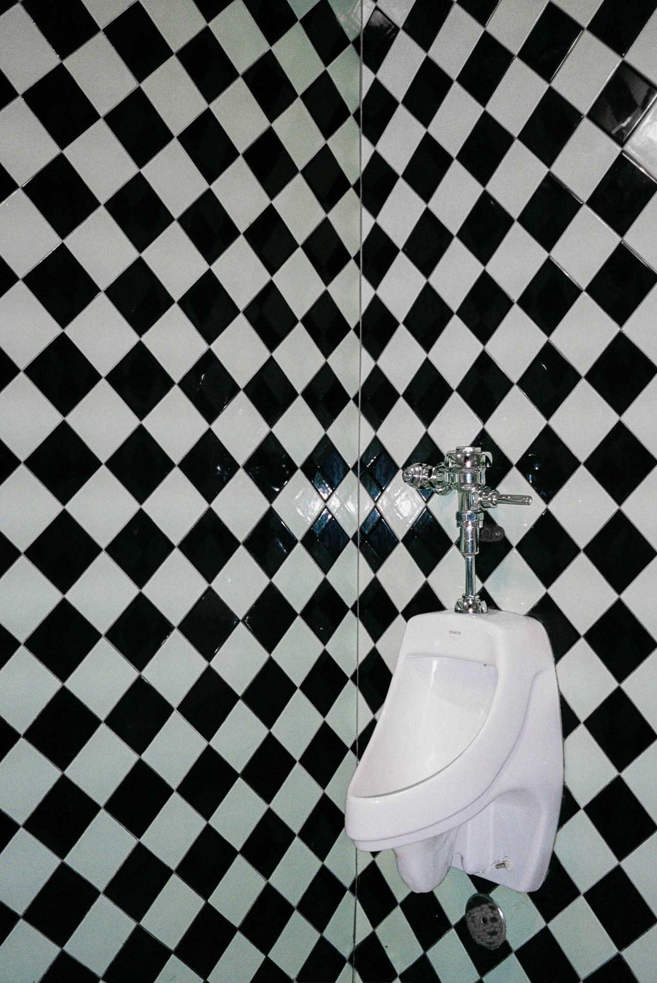 Urinal with black and white checkered in tiled bathroom. Checkers on Film from Jonathan Grado's Hold Down to Flush.