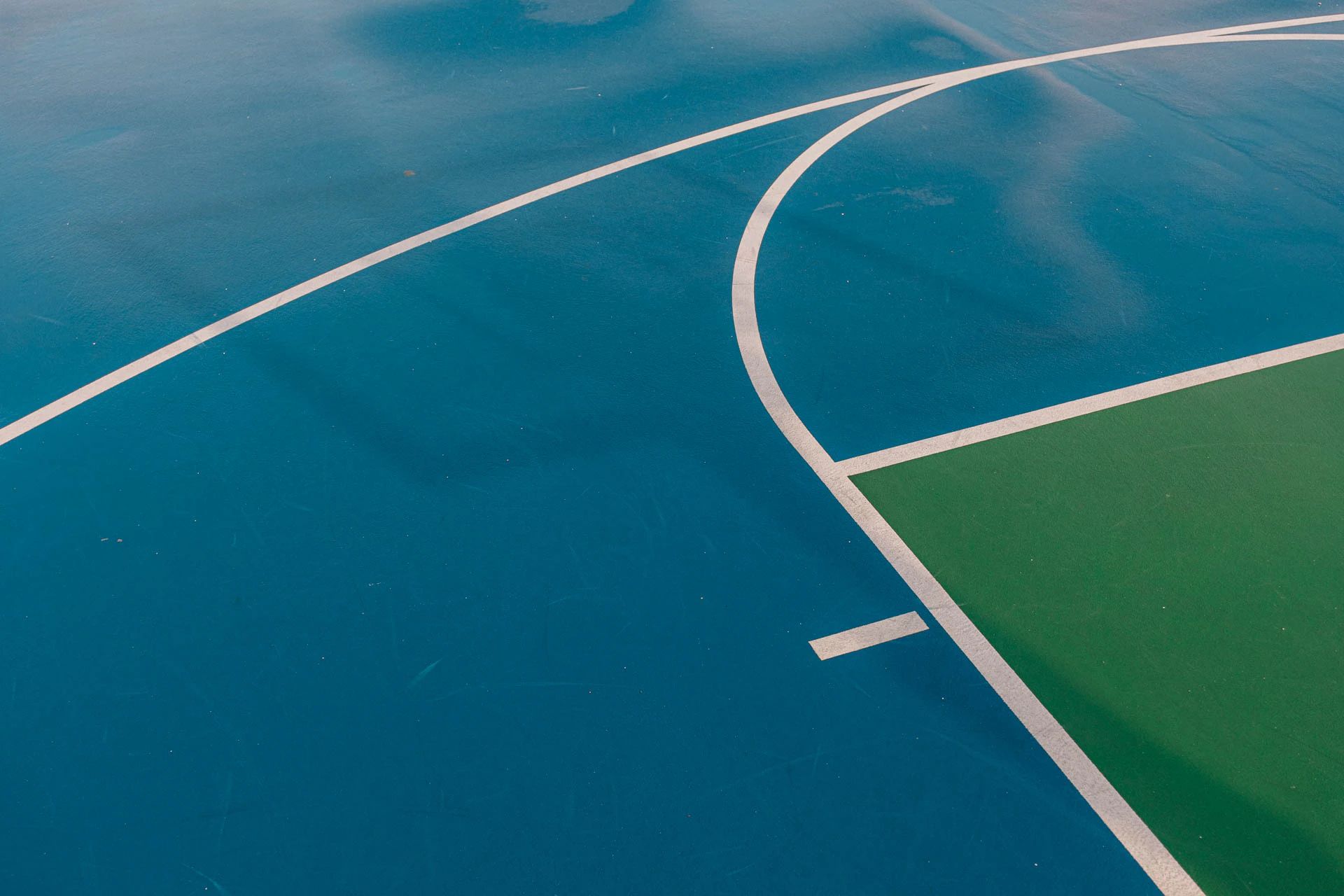 hoop shadows in the reflection of a rainy blue and green basketball court