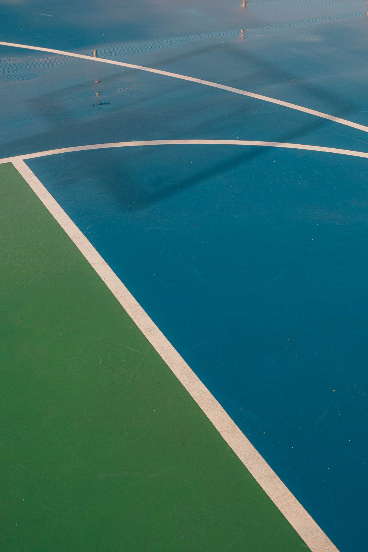 hoop shadows in the reflection of a rainy blue and green basketball court