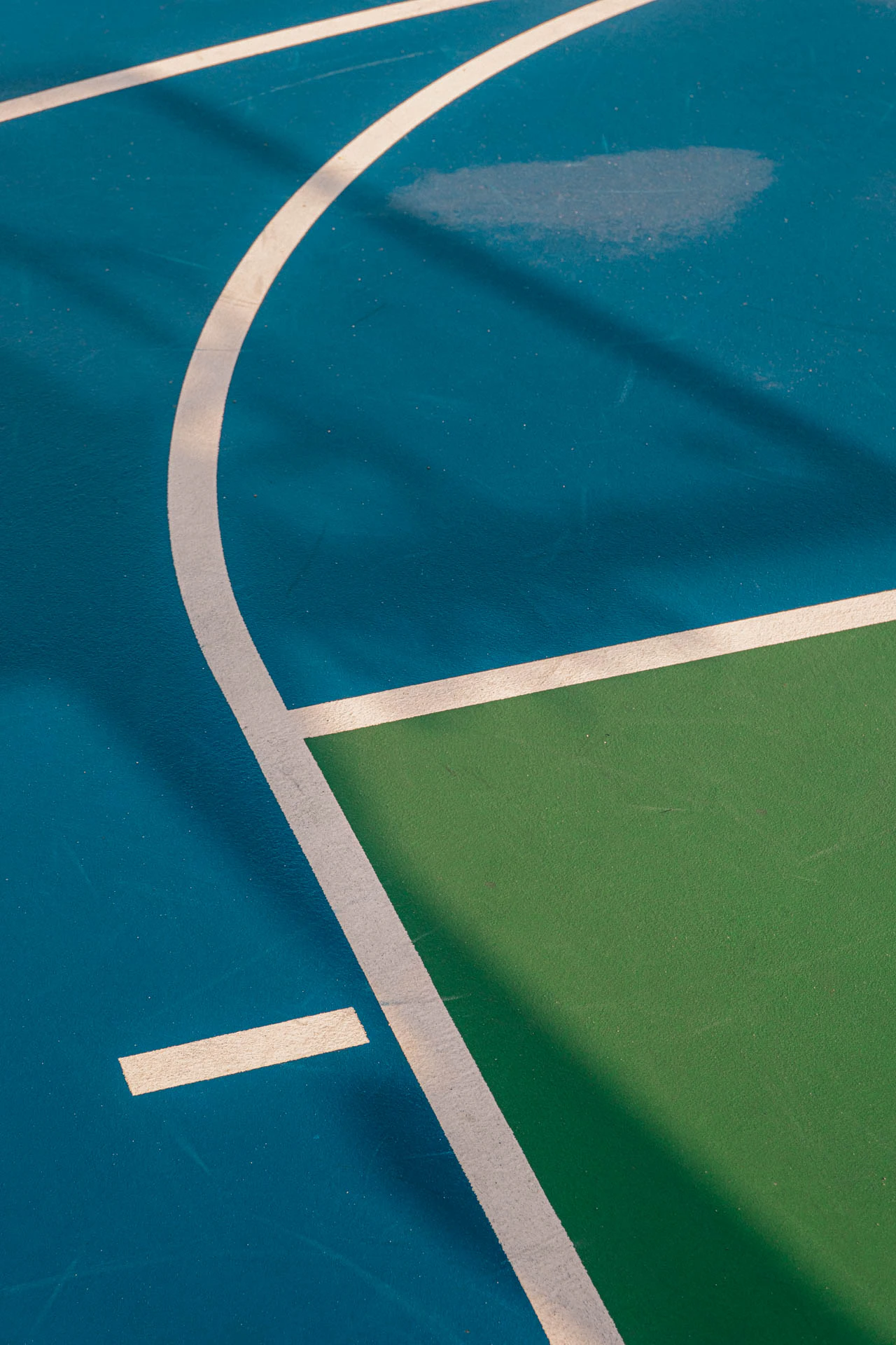 hoop shadows in the reflection of a rainy blue and green basketball court