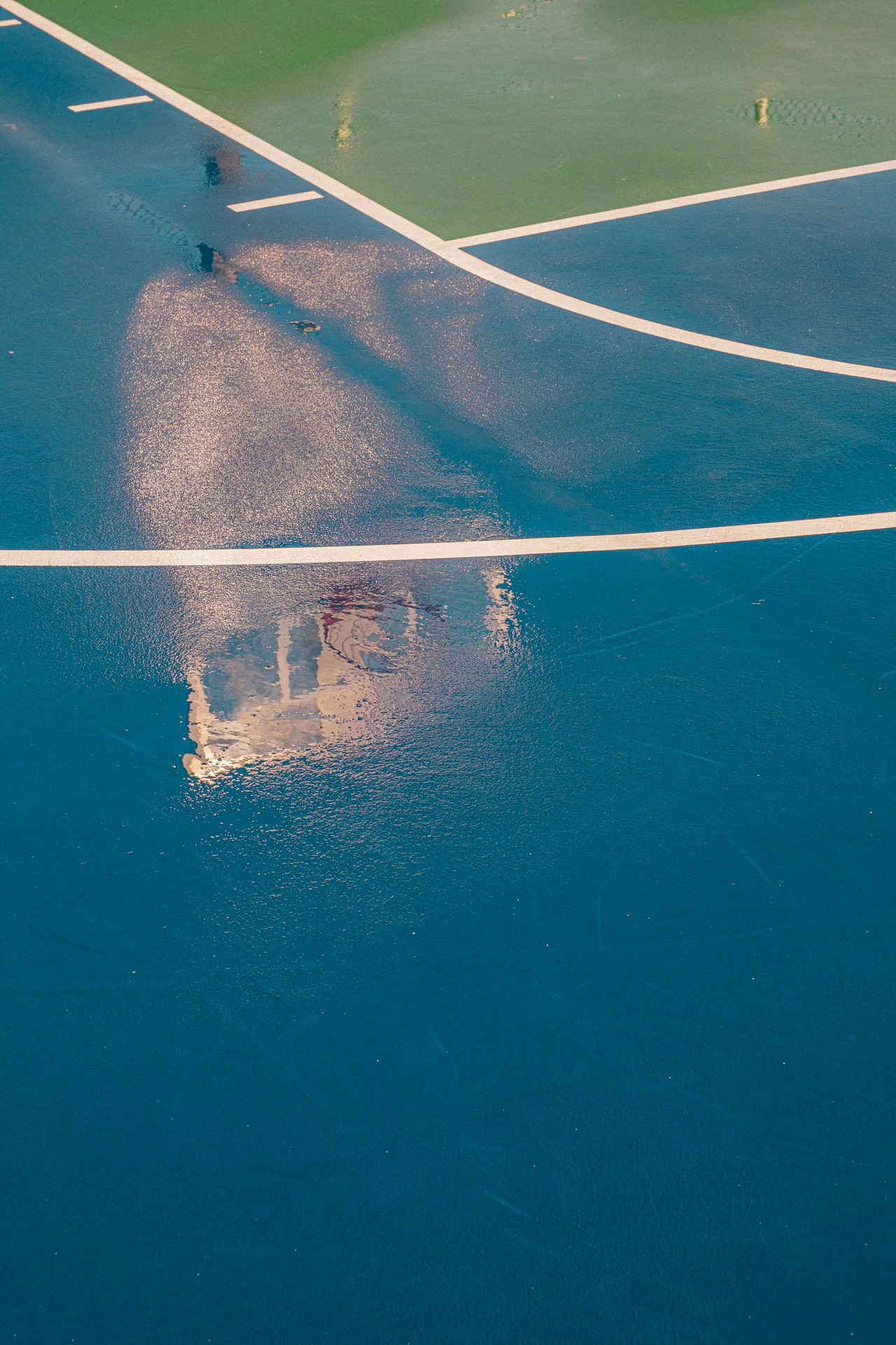 basketball hoop in the reflection of a rainy blue and green court