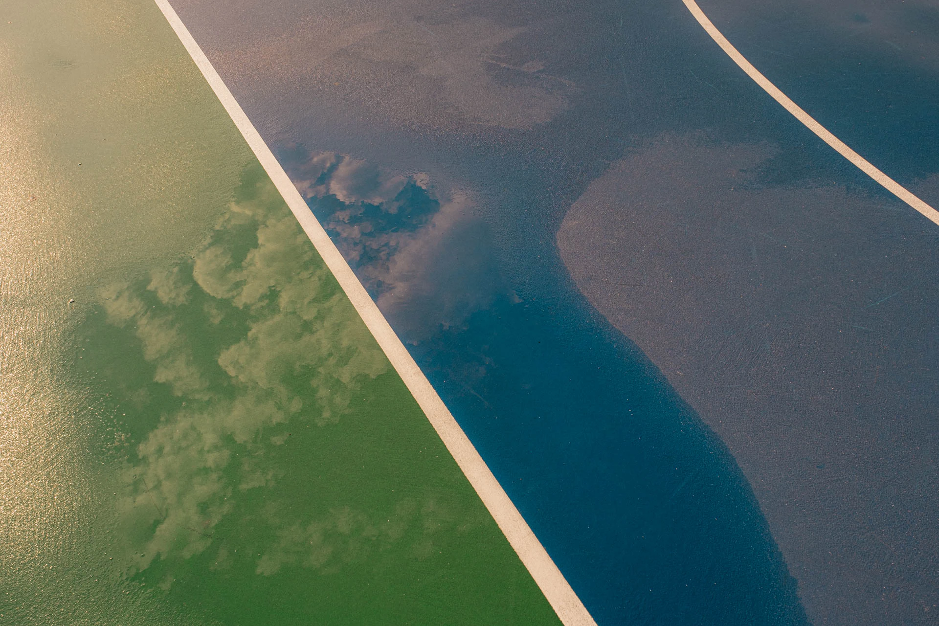 clouds in the sky in the reflection of a rainy blue and green basketball court