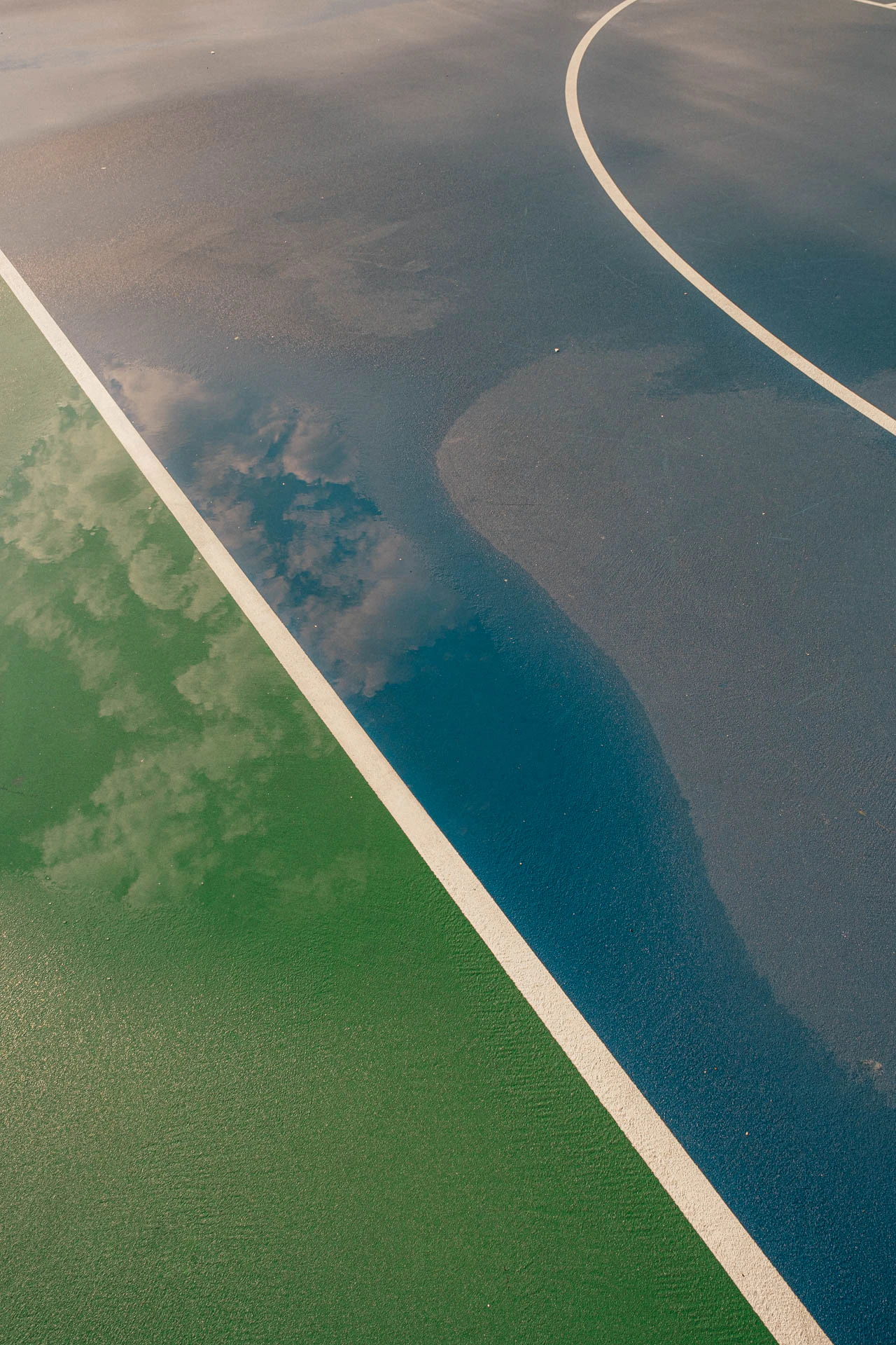 clouds in the sky in the reflection of a rainy blue and green basketball court