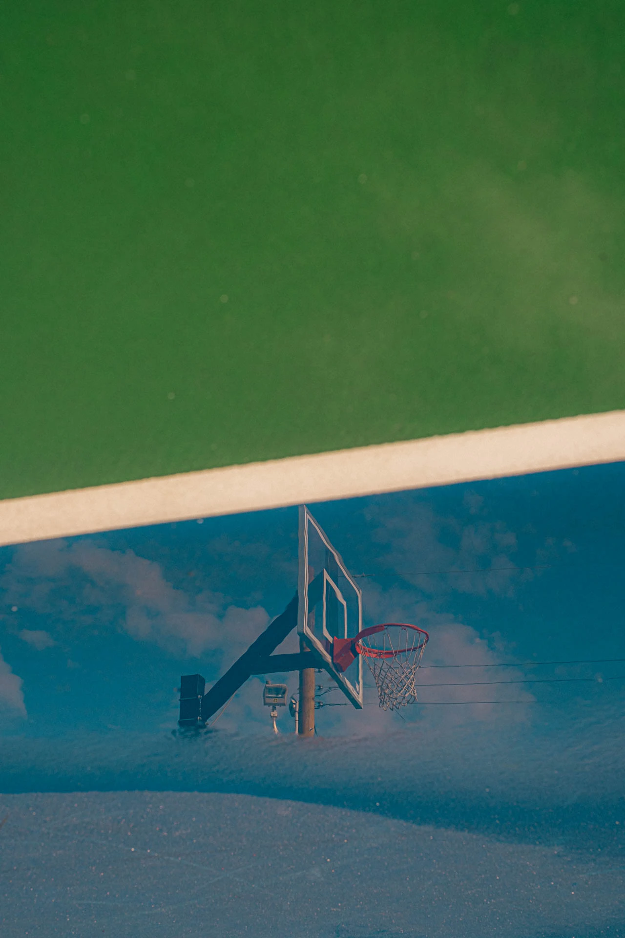 basketball hoop in the reflection of a rainy blue and green court