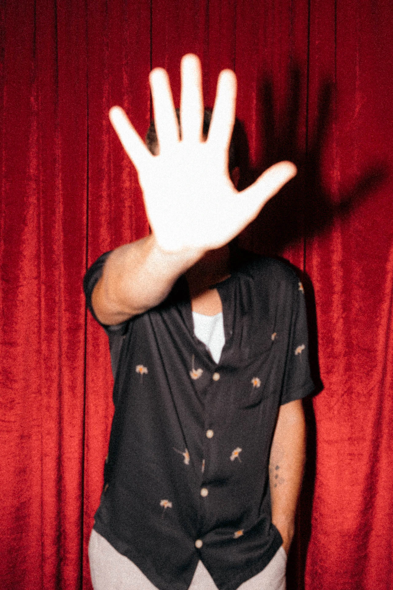 Portrait of Jonathan Grado covering his face with his hand using heightened look flash photography. Red velvet background.