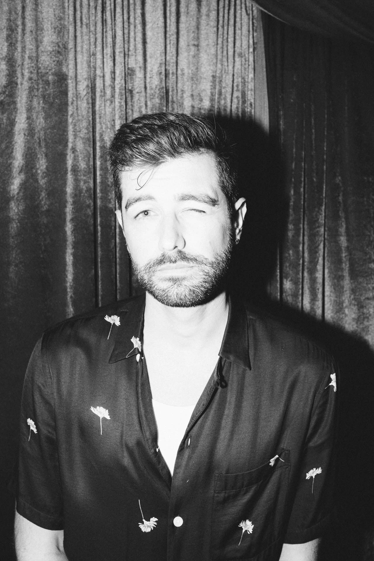 Portrait of Jonathan Grado squinting using heightened look flash photography. Black and white velvet.