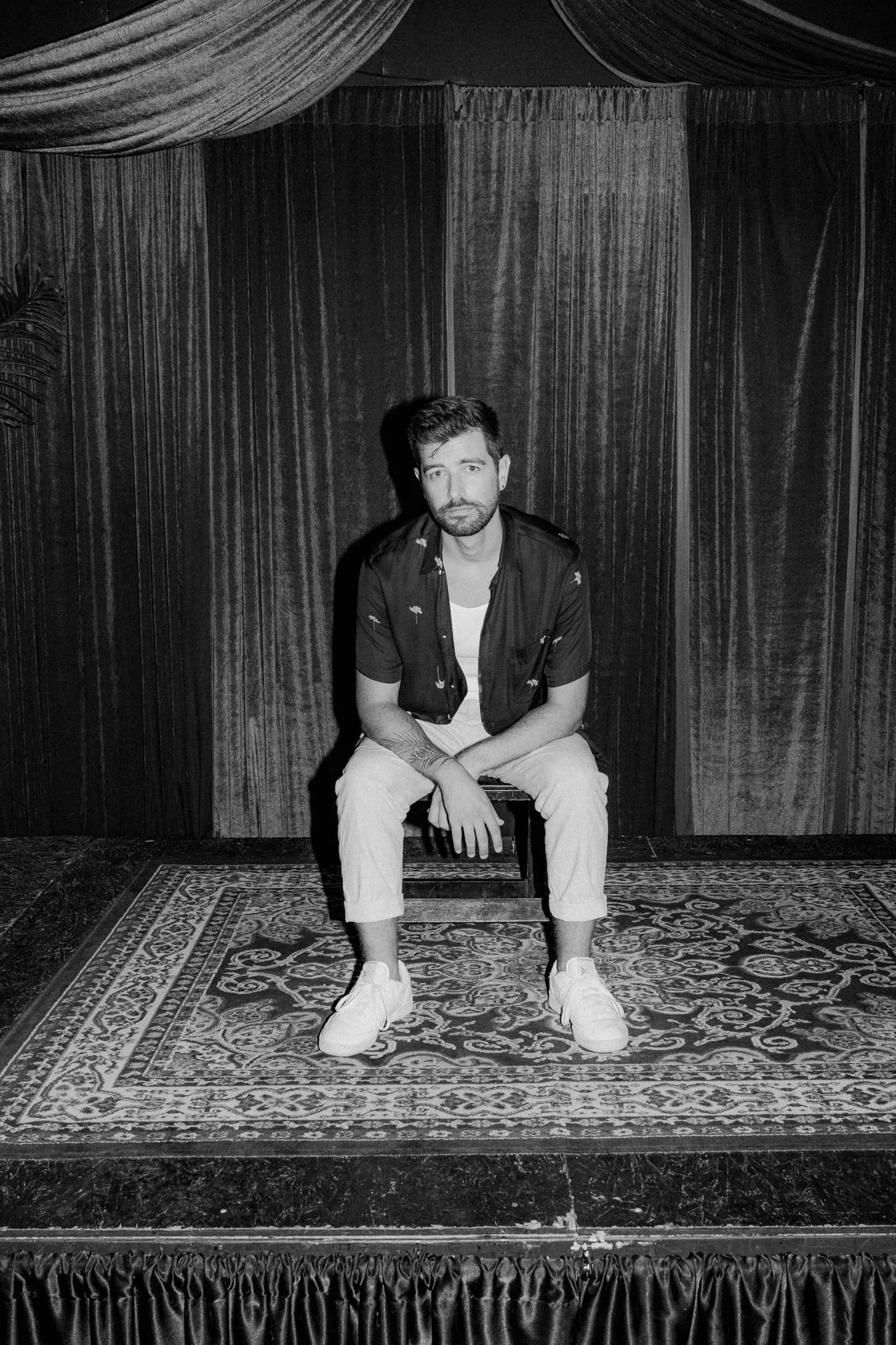 Portrait of Jonathan Grado sitting on a stage using heightened look flash photography. Black and white.