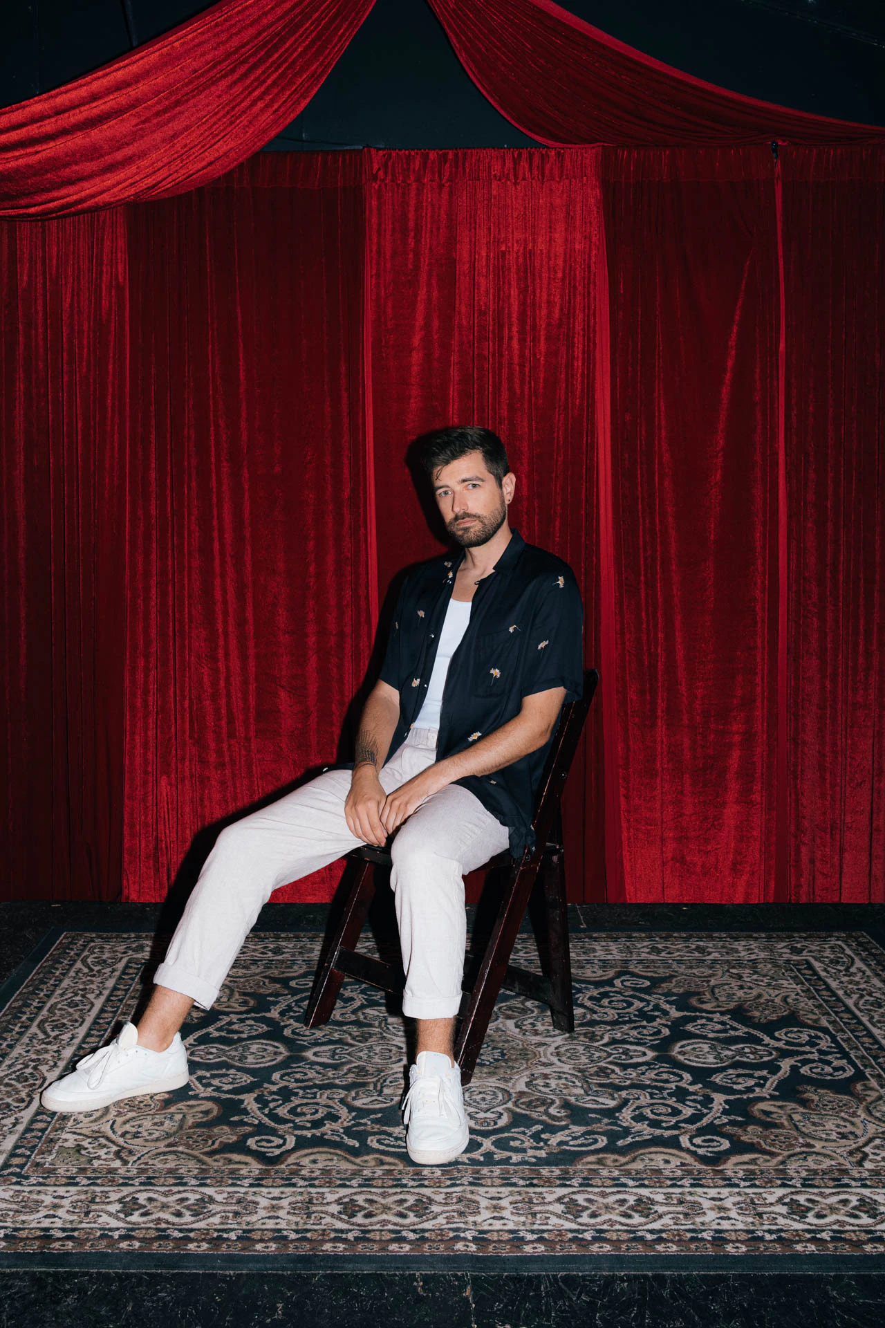Portrait of Jonathan Grado sitting on a stage using heightened look flash photography. Red velvet background.