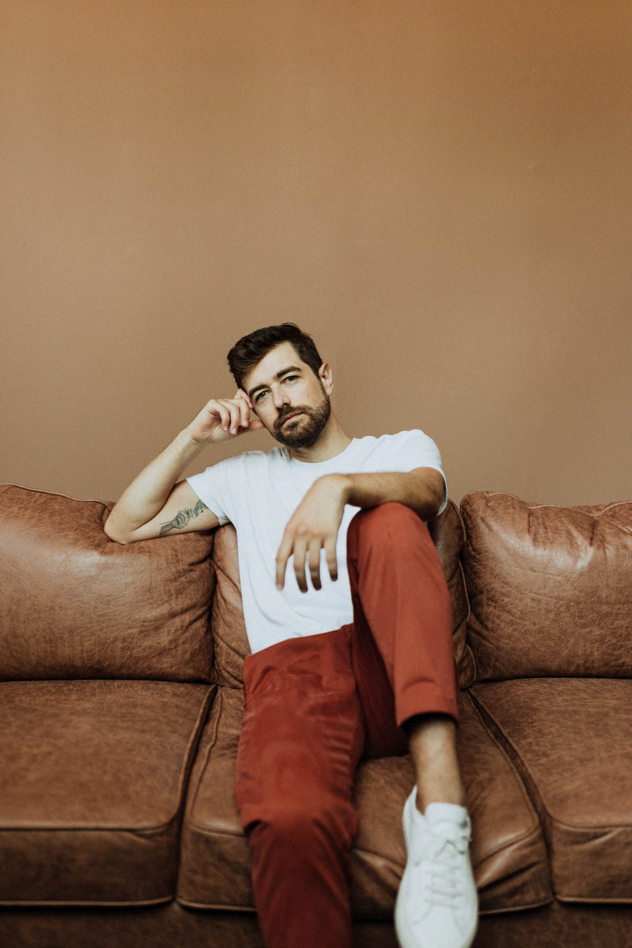portrait of Jonathan Grado sitting down on a couch in red pants with his knee up