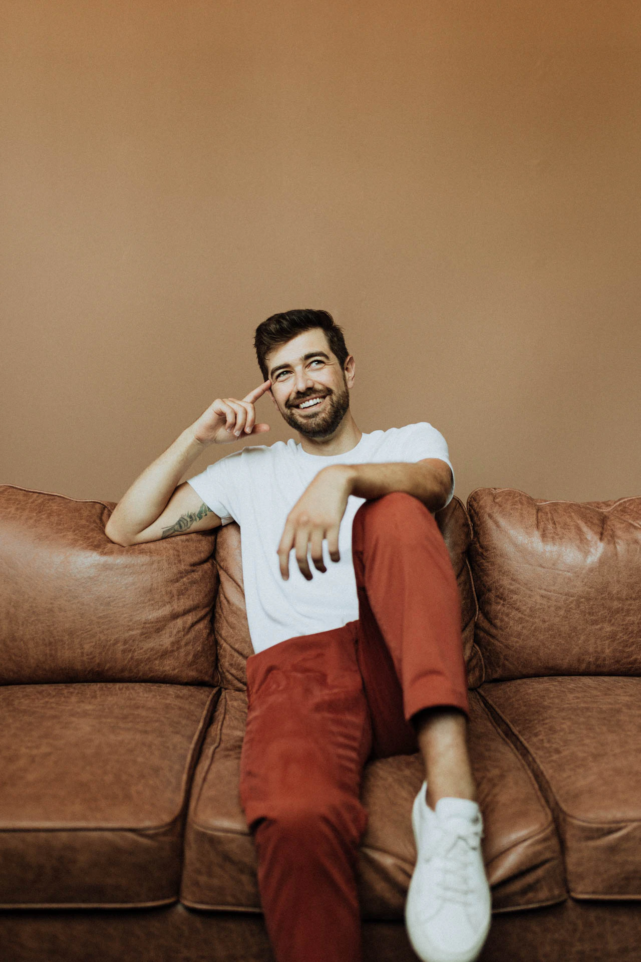 portrait of Jonathan Grado sitting down on a couch in red pants with his knee up