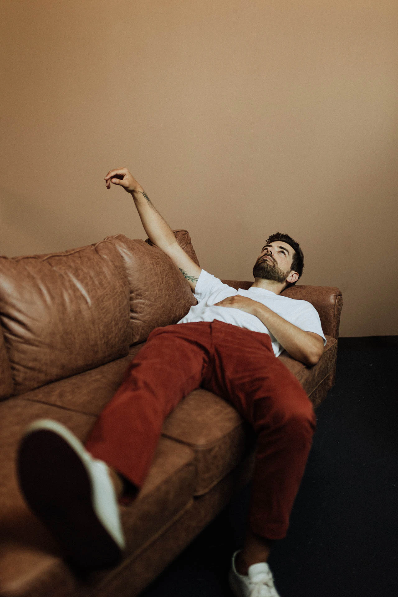 portrait of Jonathan Grado lying down on a couch in red pants with his arm in the air