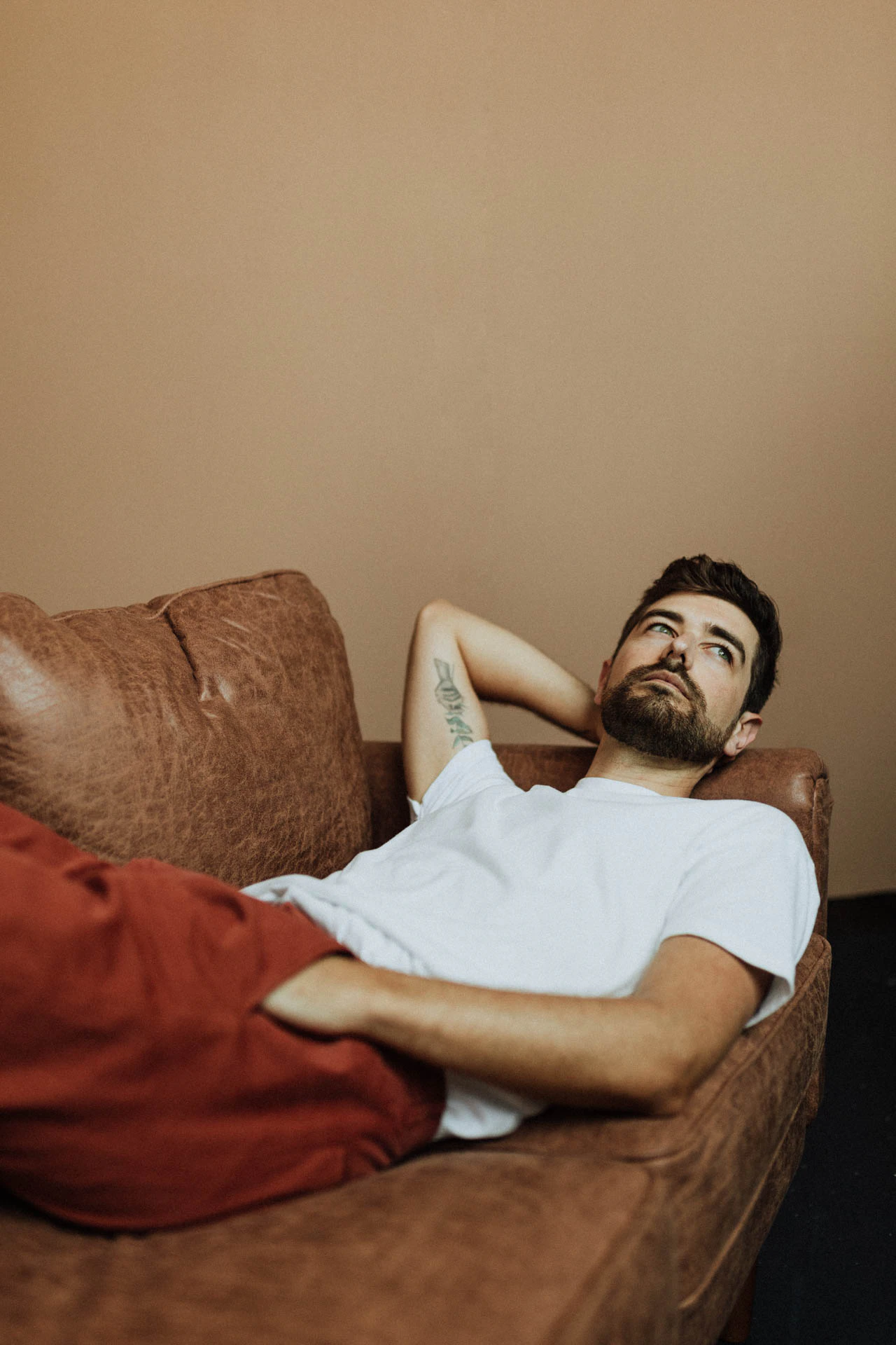 portrait of Jonathan Grado lying down on a couch in red pants with his hand in his pocket