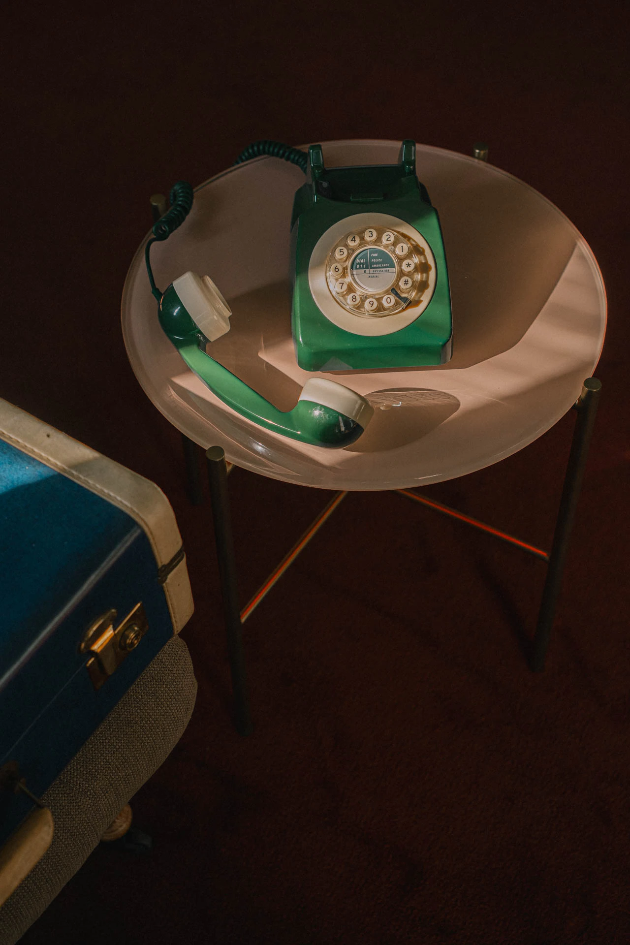An old green rotary phone with a blue briefcase. An old hotel with red carpet. Sunset.