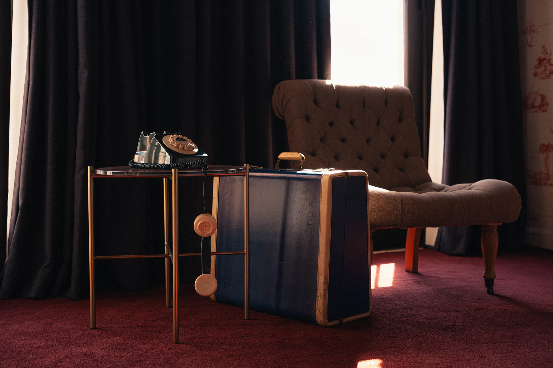 An old green rotary phone with a blue briefcase. An old hotel with red carpet. Sunset.