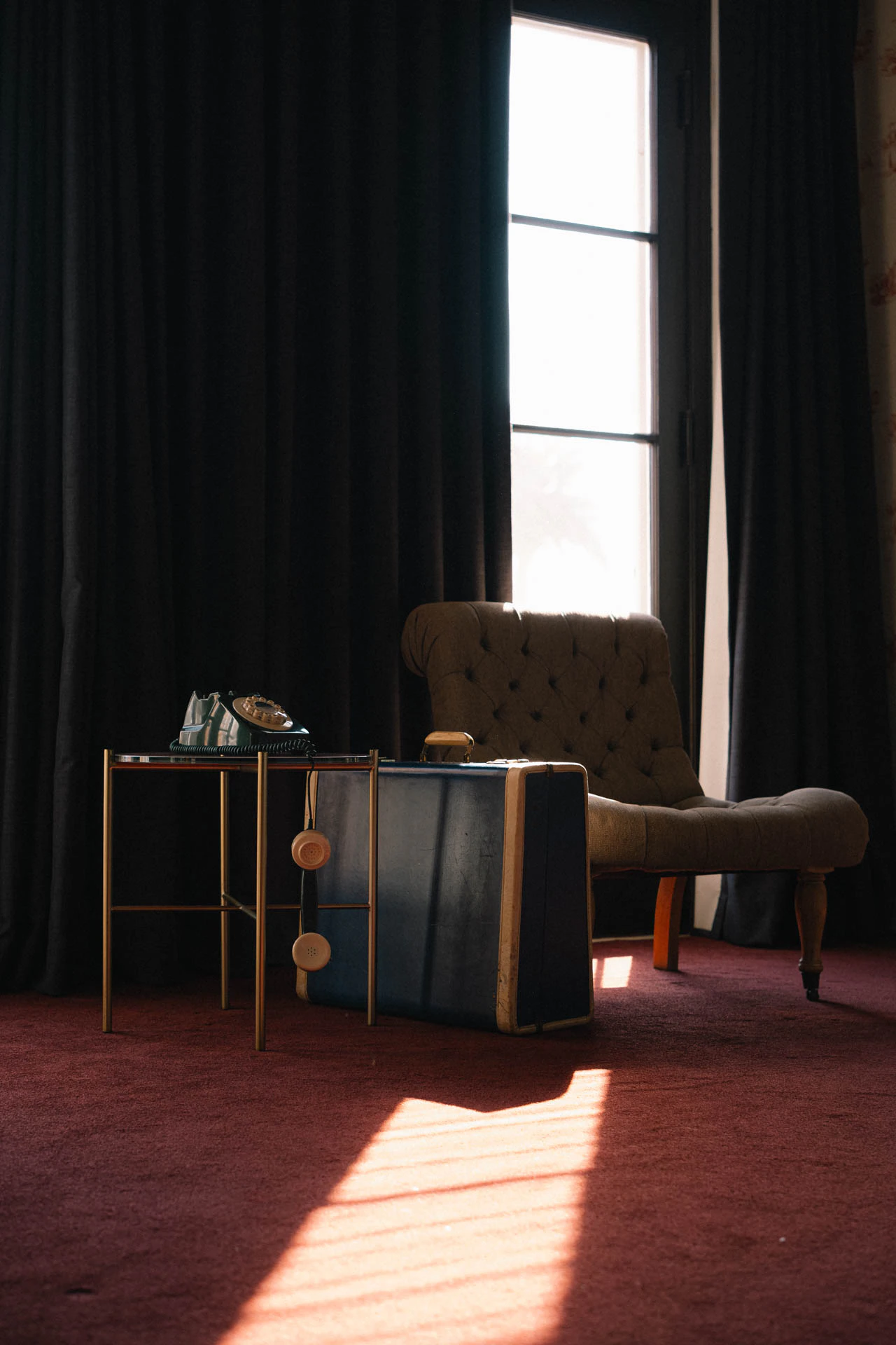 An old green rotary phone with a blue briefcase. An old hotel with red carpet. Sunset.