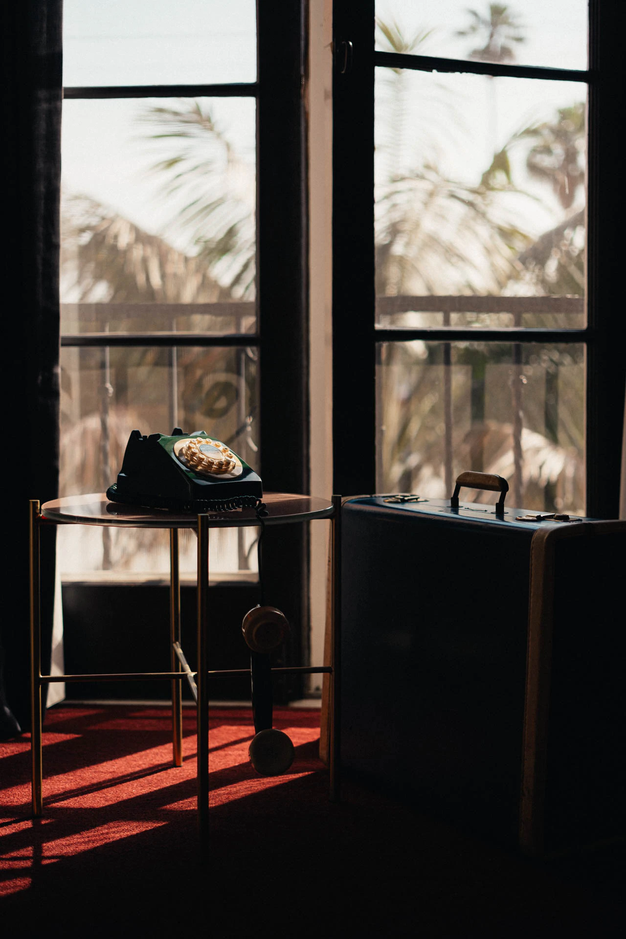 An old green rotary phone with a blue briefcase. An old hotel with red carpet. Sunset.