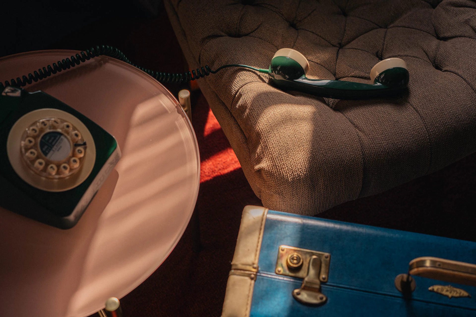 An old green rotary phone with a blue briefcase. An old hotel with red carpet. Sunset.