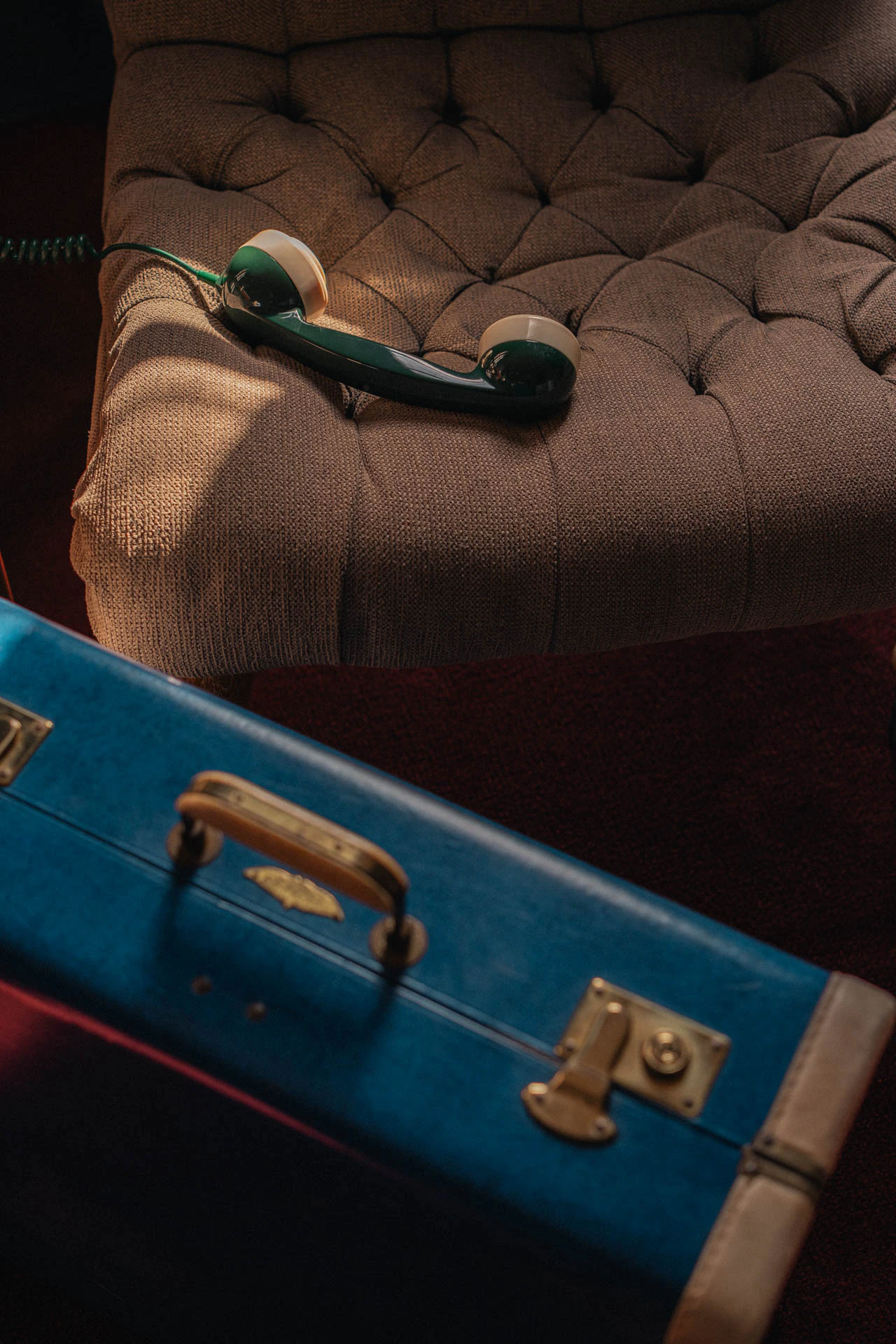 An old green rotary phone with a blue briefcase. An old hotel with red carpet. Sunset.