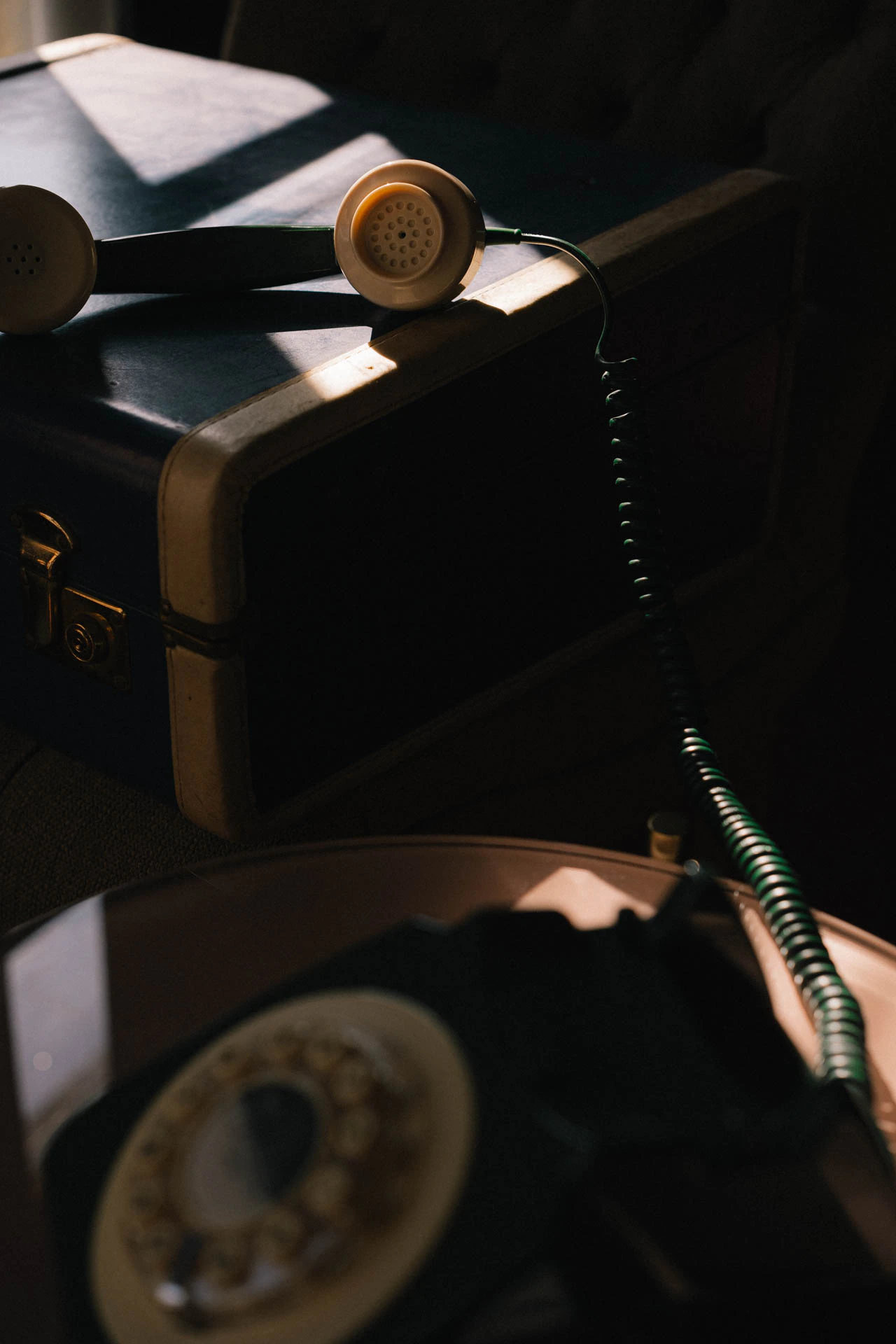 An old green rotary phone with a blue briefcase. An old hotel with red carpet. Sunset.
