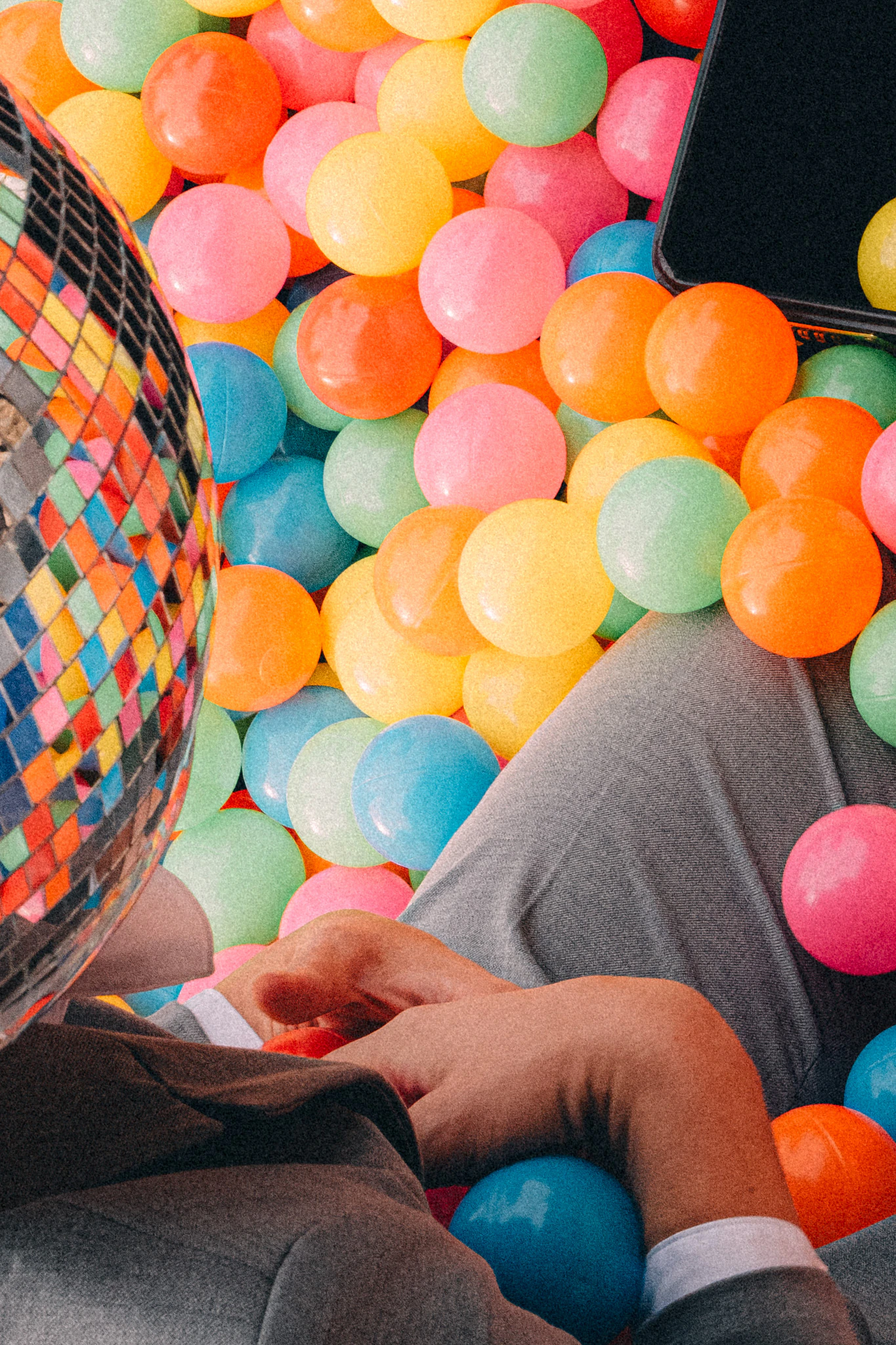 A person in a suit and disco ball for a head picking up colorful balls. Backlog from Jonathan Grado's Happy Hour series.