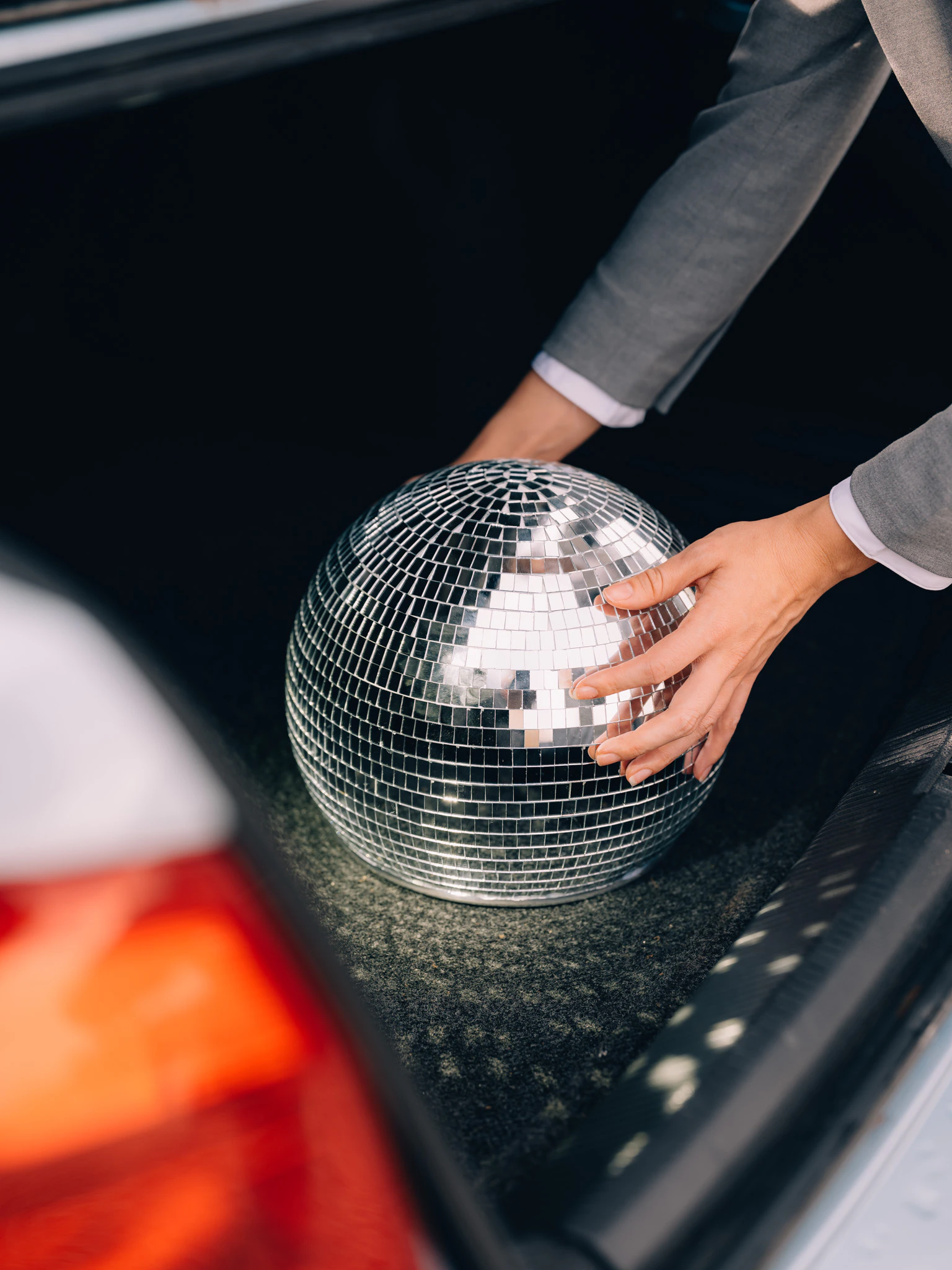 Hands reaching for a disco ball in the trunk of a car. Company Uniform from Jonathan Grado's Happy Hour series.