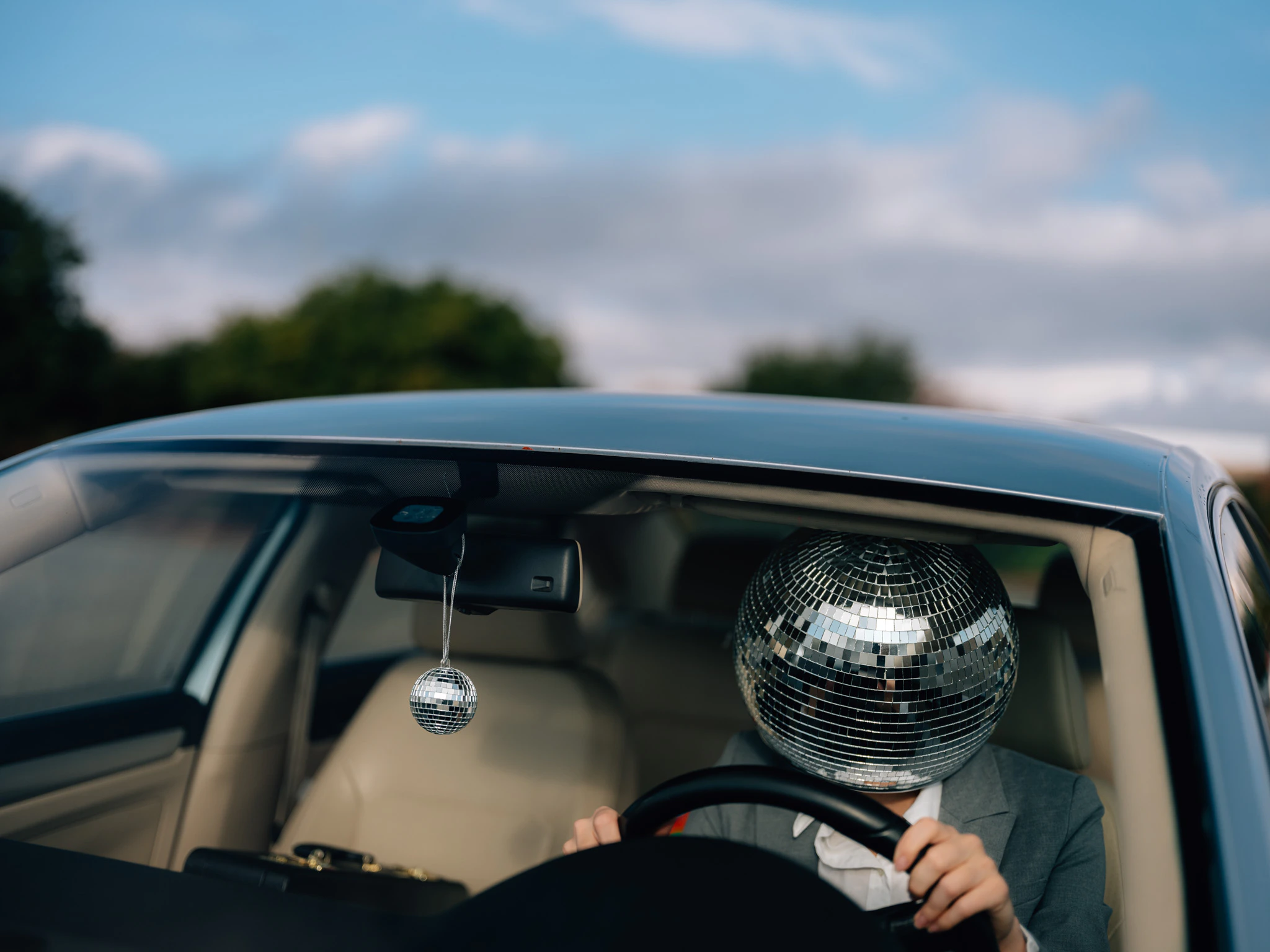 A person in a suit and disco ball for a head driving to work. Commute #01 from Jonathan Grado's Happy Hour series.