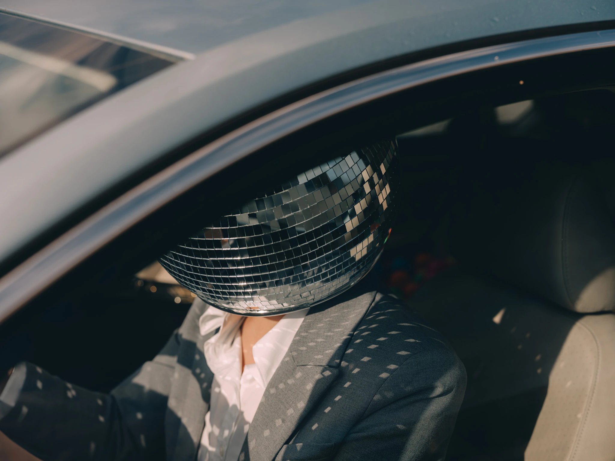 A person in a suit and disco ball for a head driving to work. Commute #02 from Jonathan Grado's Happy Hour series.