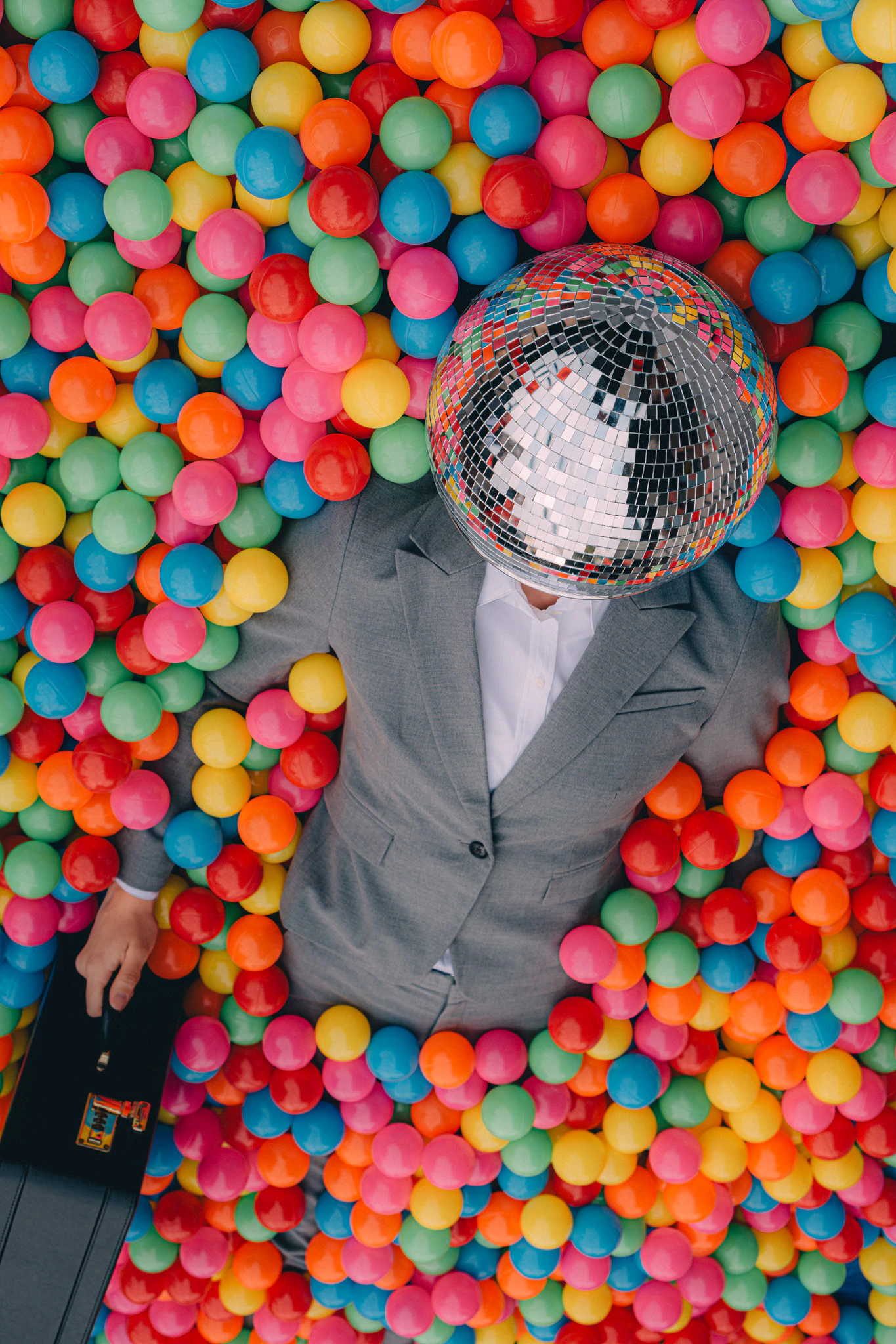 A person in a suit and disco ball for a head coming out of a colorful ball pit. Happy Hour from Jonathan Grado's Happy Hour series.