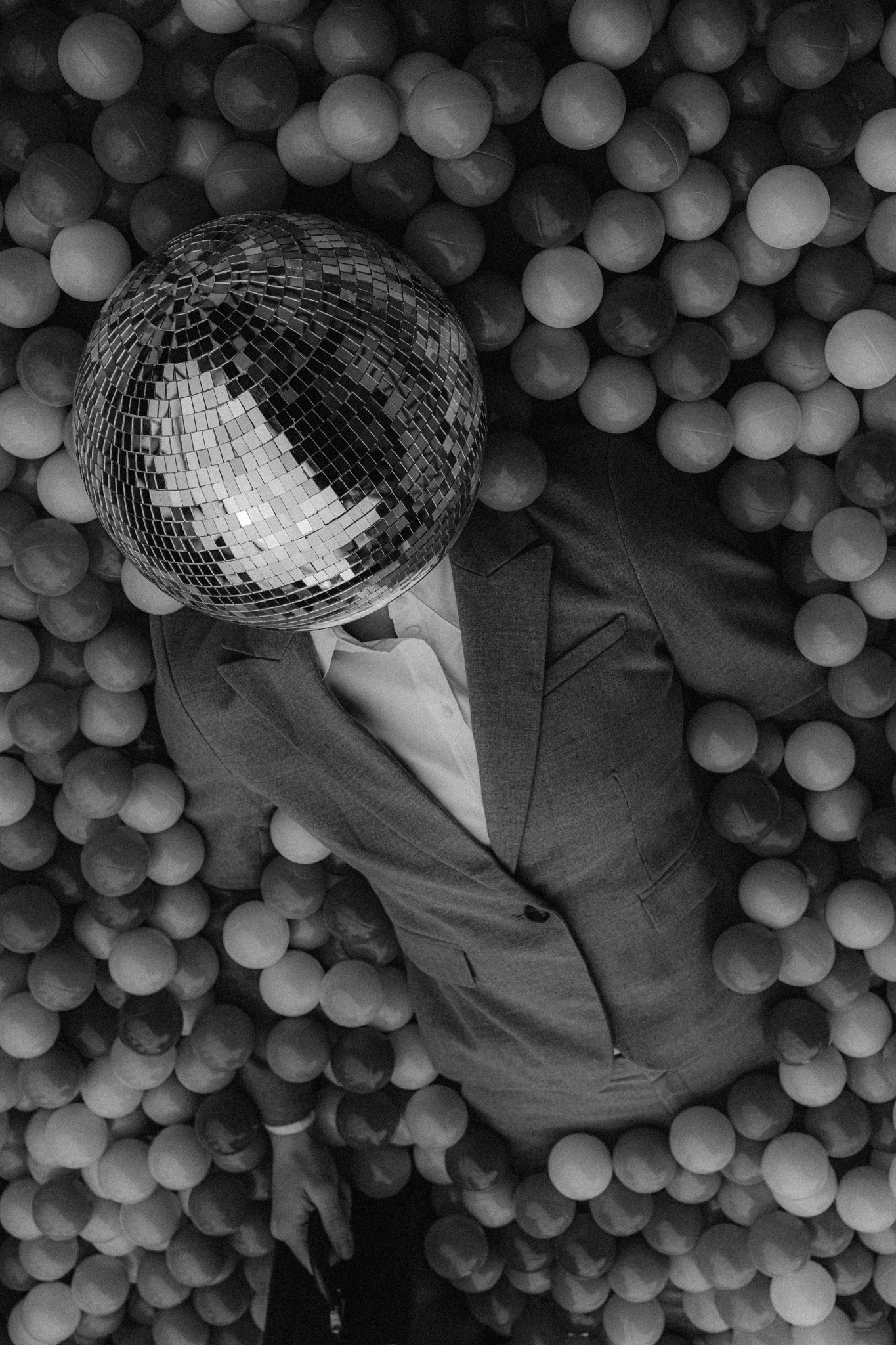 A person in a suit and disco ball for a head emerging out of a black and white ball pit. Fully Vested from Jonathan Grado's Happy Hour series.