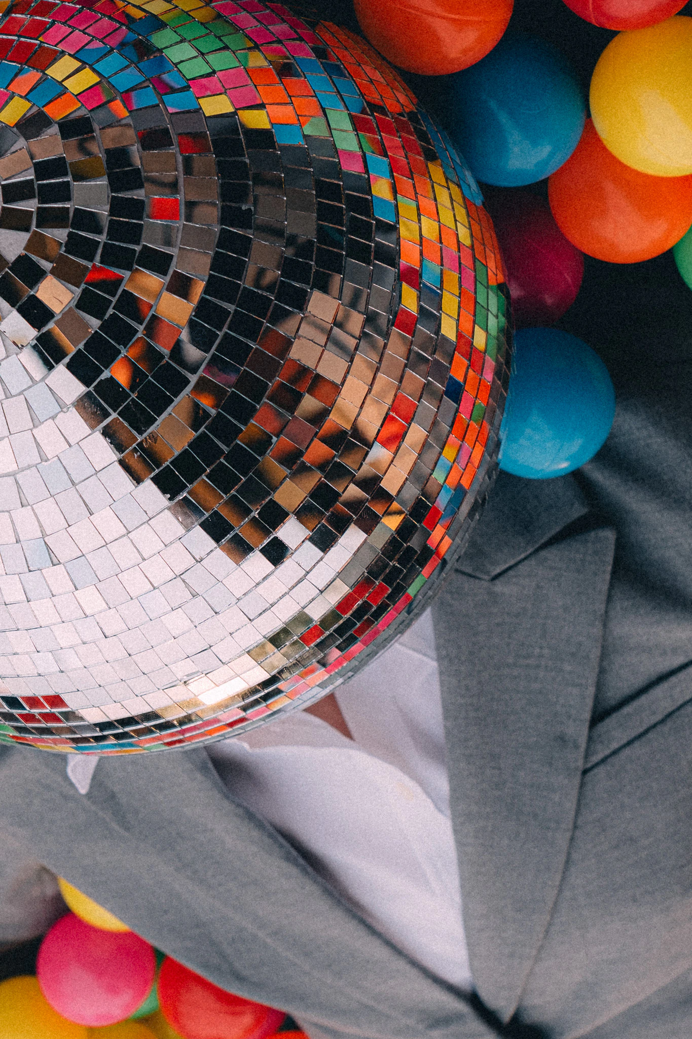 A person in a suit and disco ball head reflecting a colorful ball pit. New Hire from Jonathan Grado's Happy Hour series.
