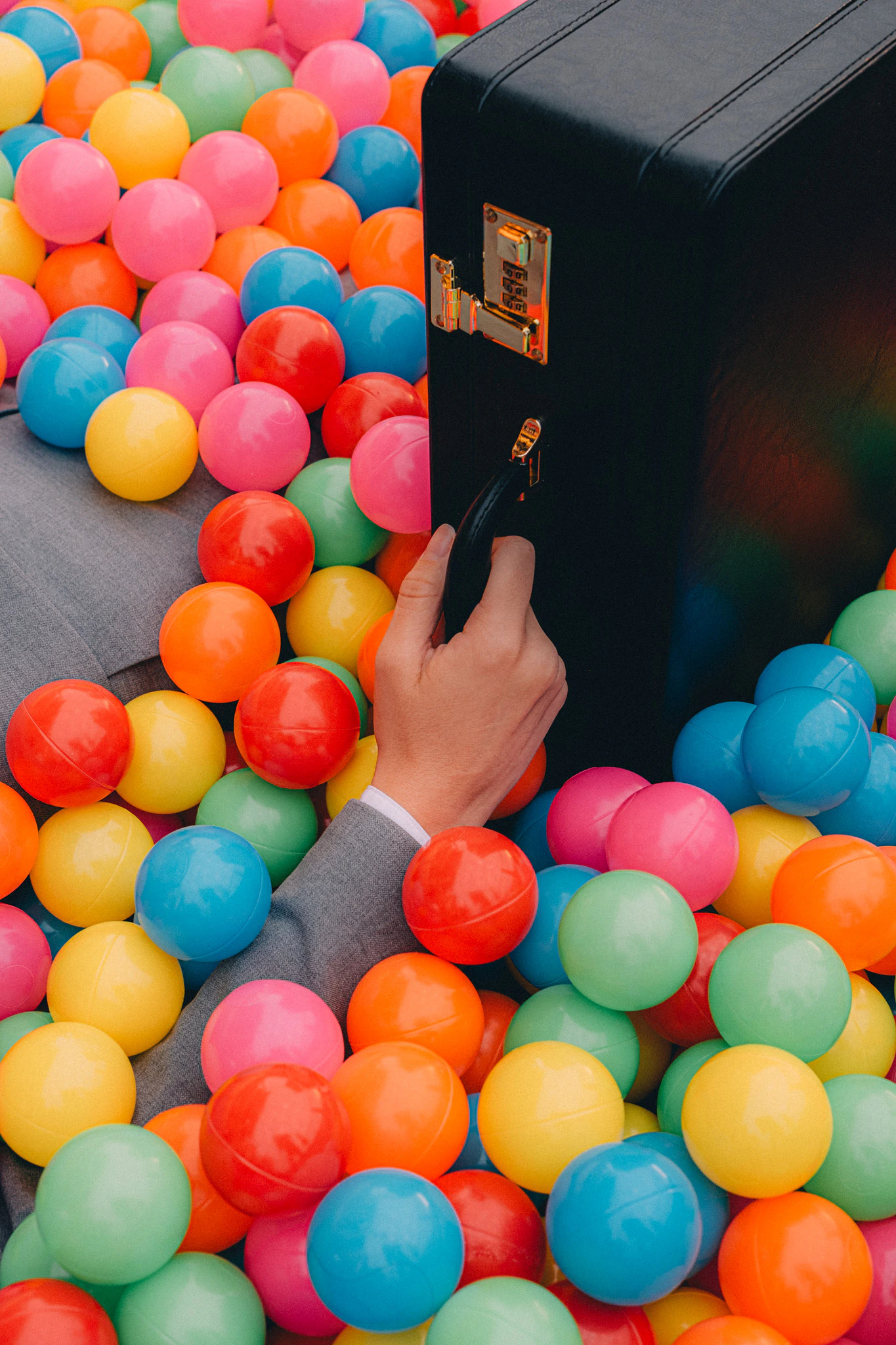 A businessman in a suit and their hand is holding a briefcase in a colorful ball pit. Onboarding from Jonathan Grado's Happy Hour series.