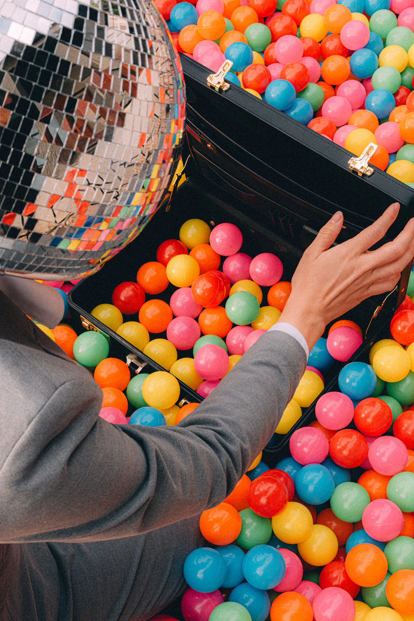 A colorful ball pit with a person in a suit and disco ball for a head opening their briefcase. Seasoned Associate from Jonathan Grado's Happy Hour series.