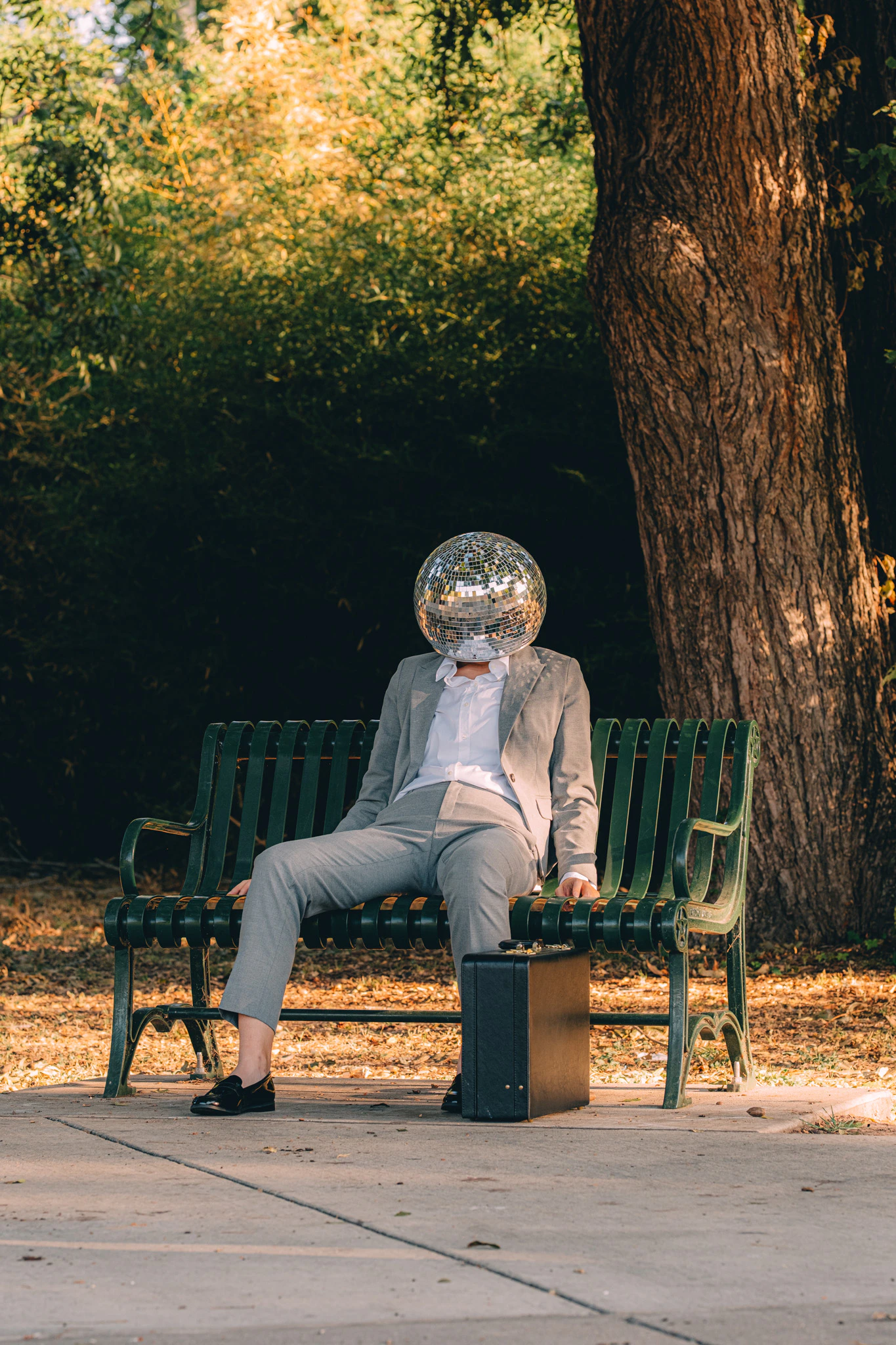 A person in a suit and disco ball for a head slouching on a park bench. The Quiet Resignation of Disco Ball Head.