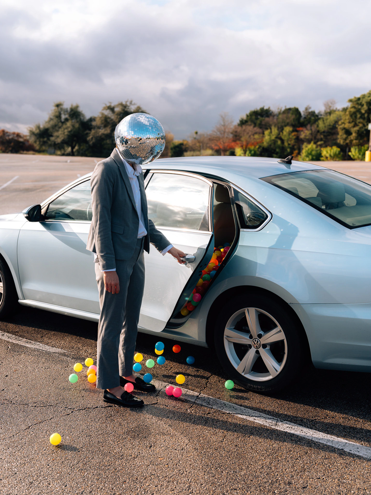 A disco ball headed person opening their car door to a ball pit. Vested Interest from Jonathan Grado's Happy Hour series.