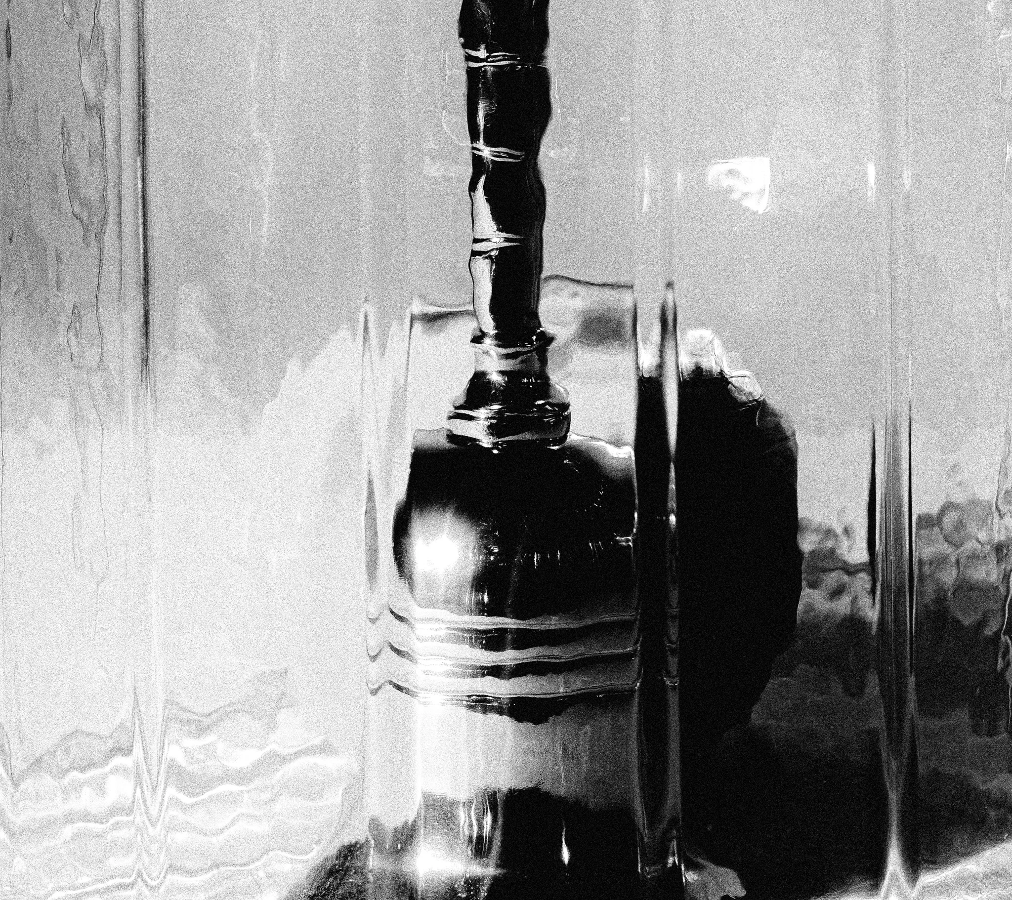 A close-up of an orange behind a small hand bell in a glass dome in black and white. Ego from Jonathan Grado's Saint Citrus series.