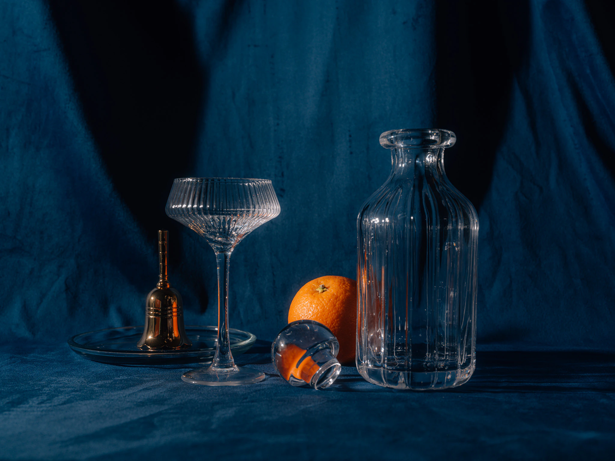 An orange behind different shaped glass on blue velvet. Compartments from Jonathan Grado's Saint Citrus series.