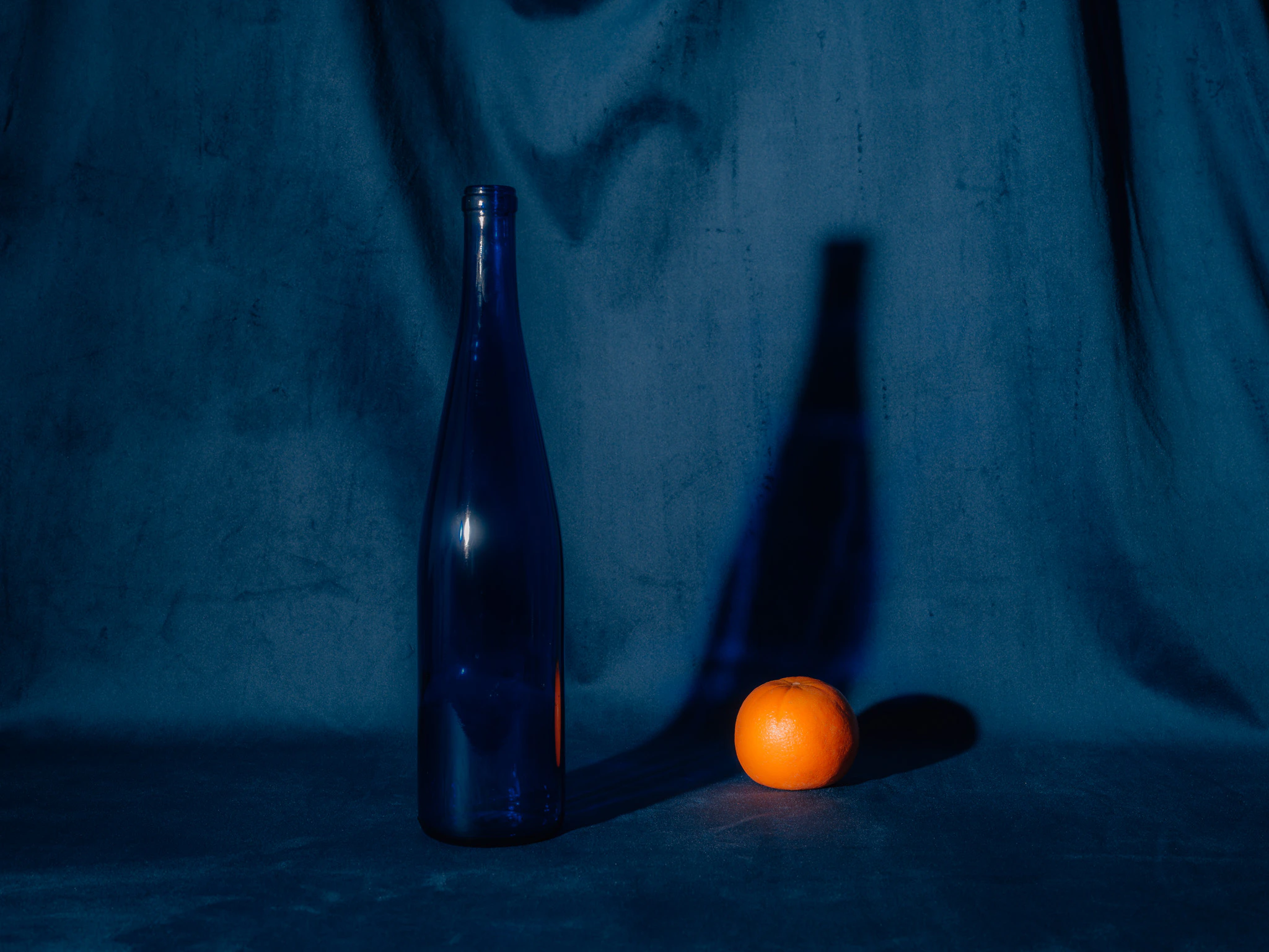 An orange with a blue glass bottle on blue velvet. Constant Comparison from Jonathan Grado's Saint Citrus series.