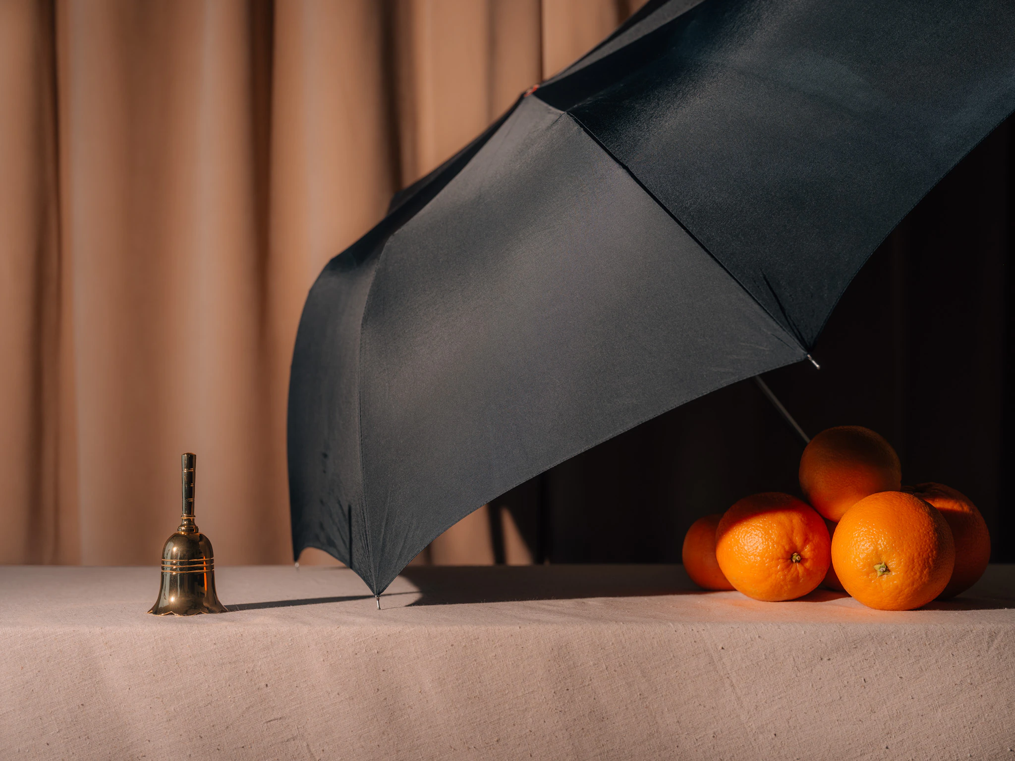 Oranges covered by an umbrella in front of a small bell in front of beige velvet. I Used to Have Good Ideas #01 from Jonathan Grado's Saint Citrus series.