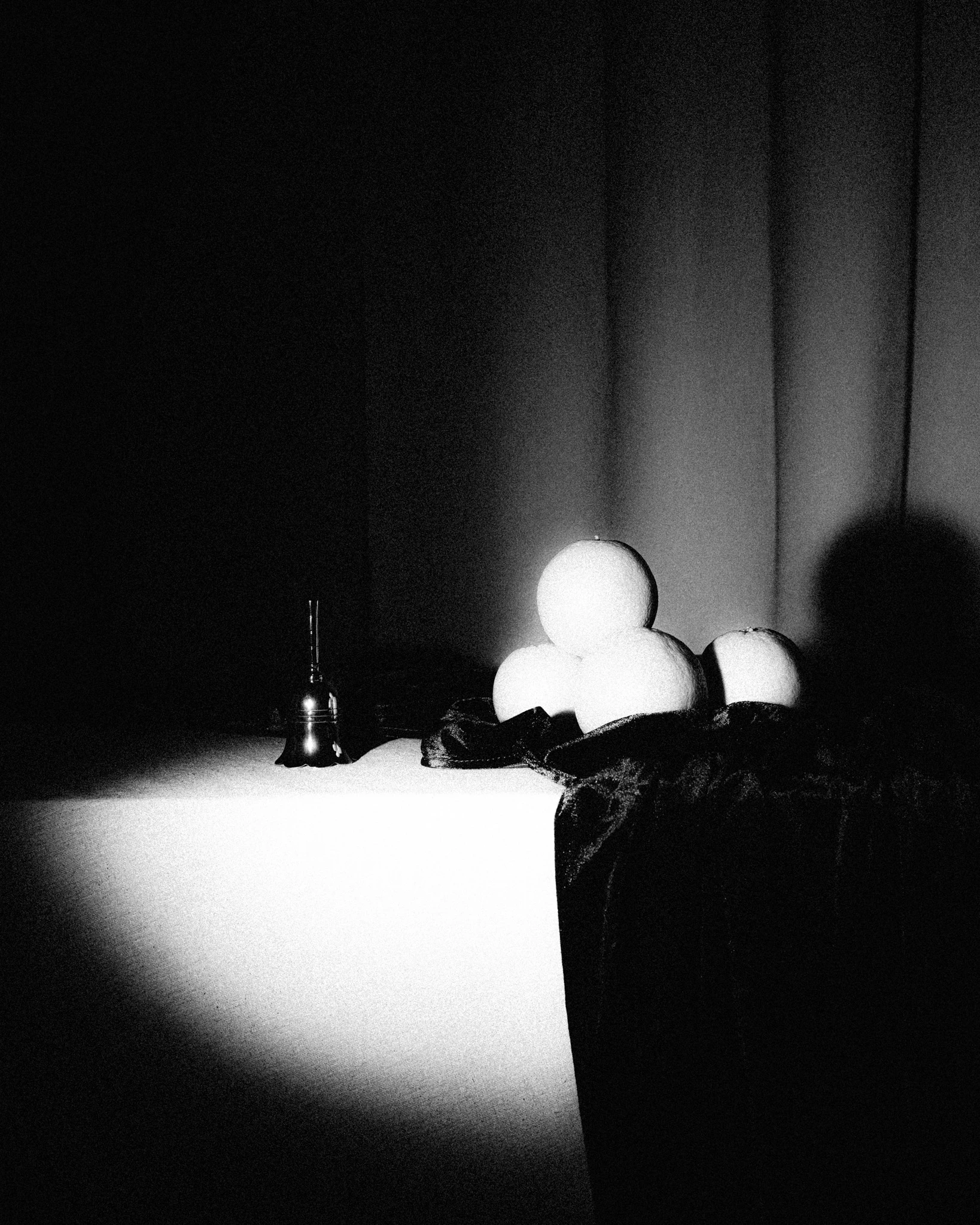 A handbell and stack of oranges are overexposed by a spotlight. Fuzzy on the Script from Jonathan Grado's Saint Citrus series.